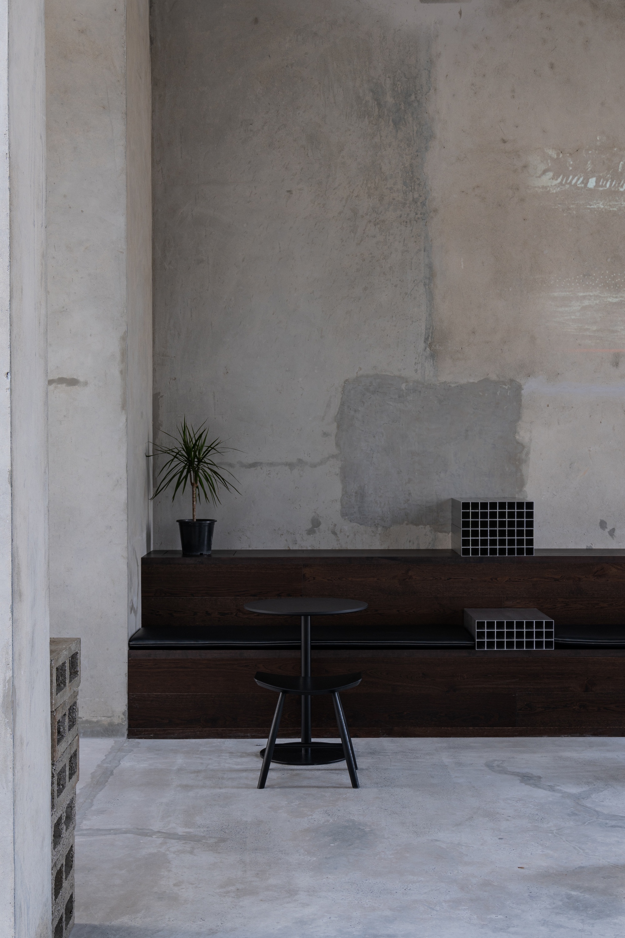 Dark timber bench against patched concrete wall with a small potted plant and metal stool