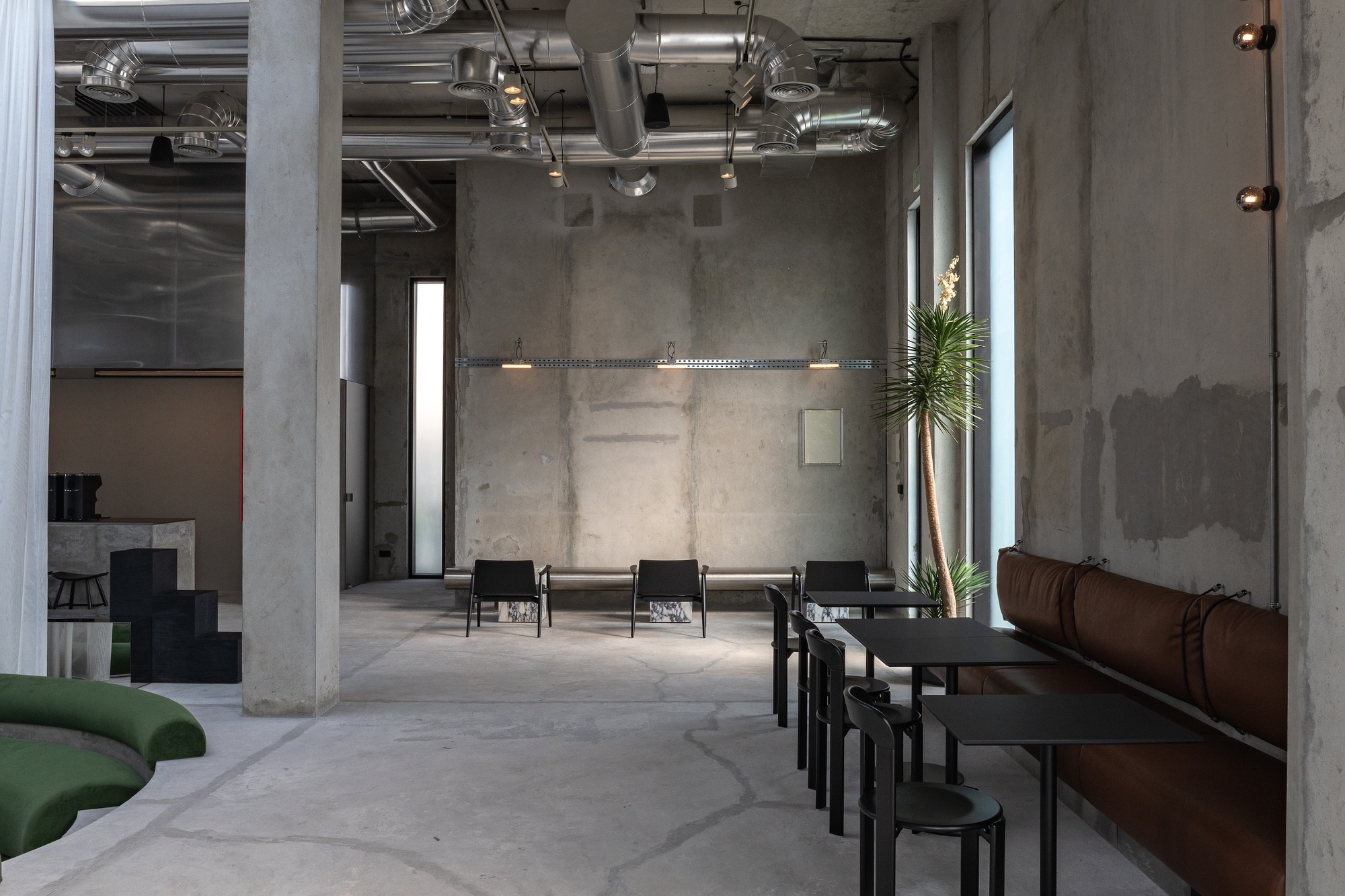 Row of low tables and stools along leather banquette seating with tall plant beside window