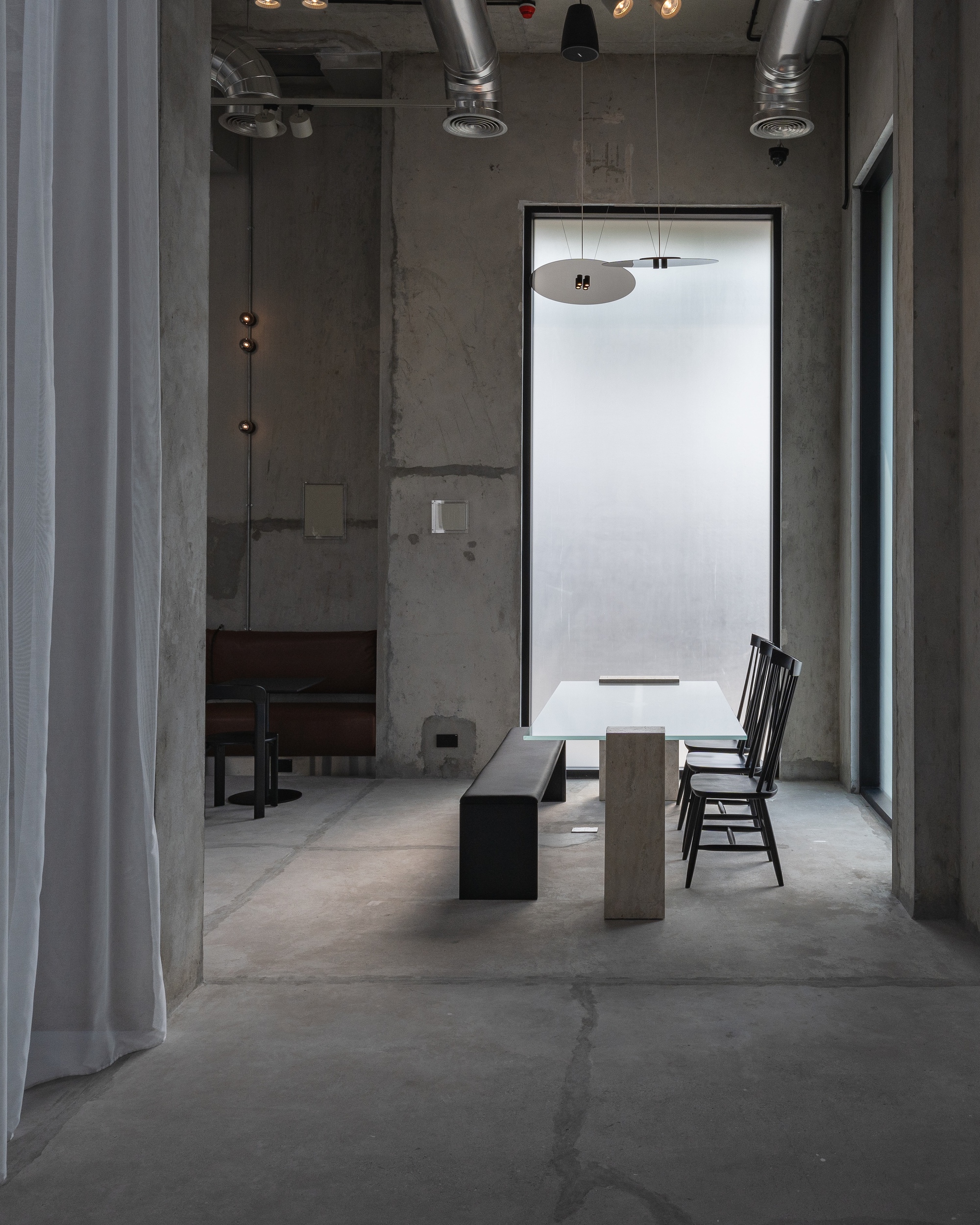 Single table with bench and chair beneath a frosted window with pendant light overhead