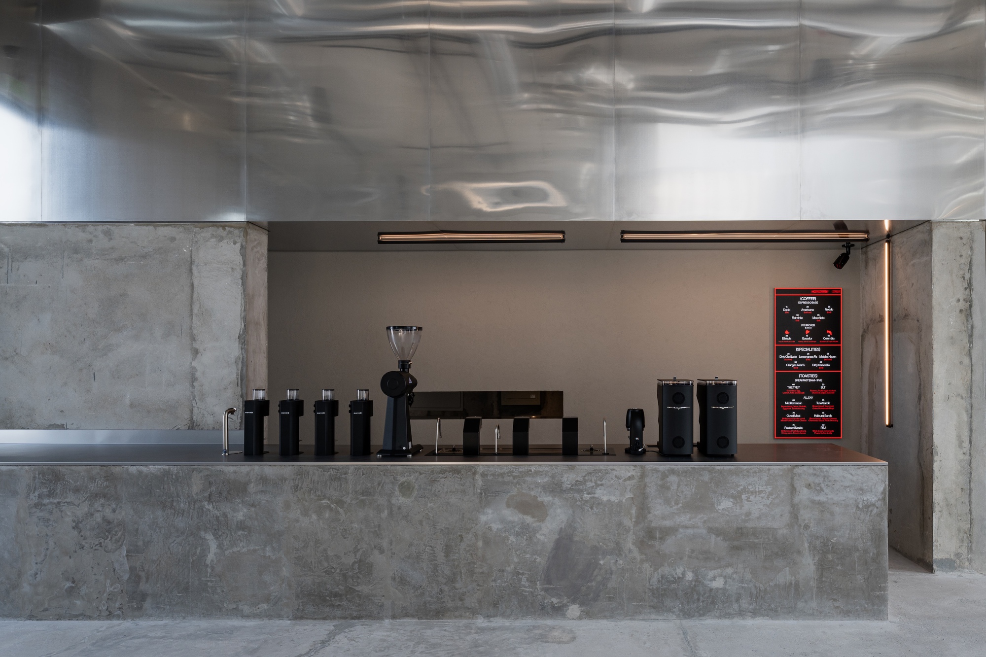 Concrete and stainless steel service counter with coffee equipment below a reflective ceiling
