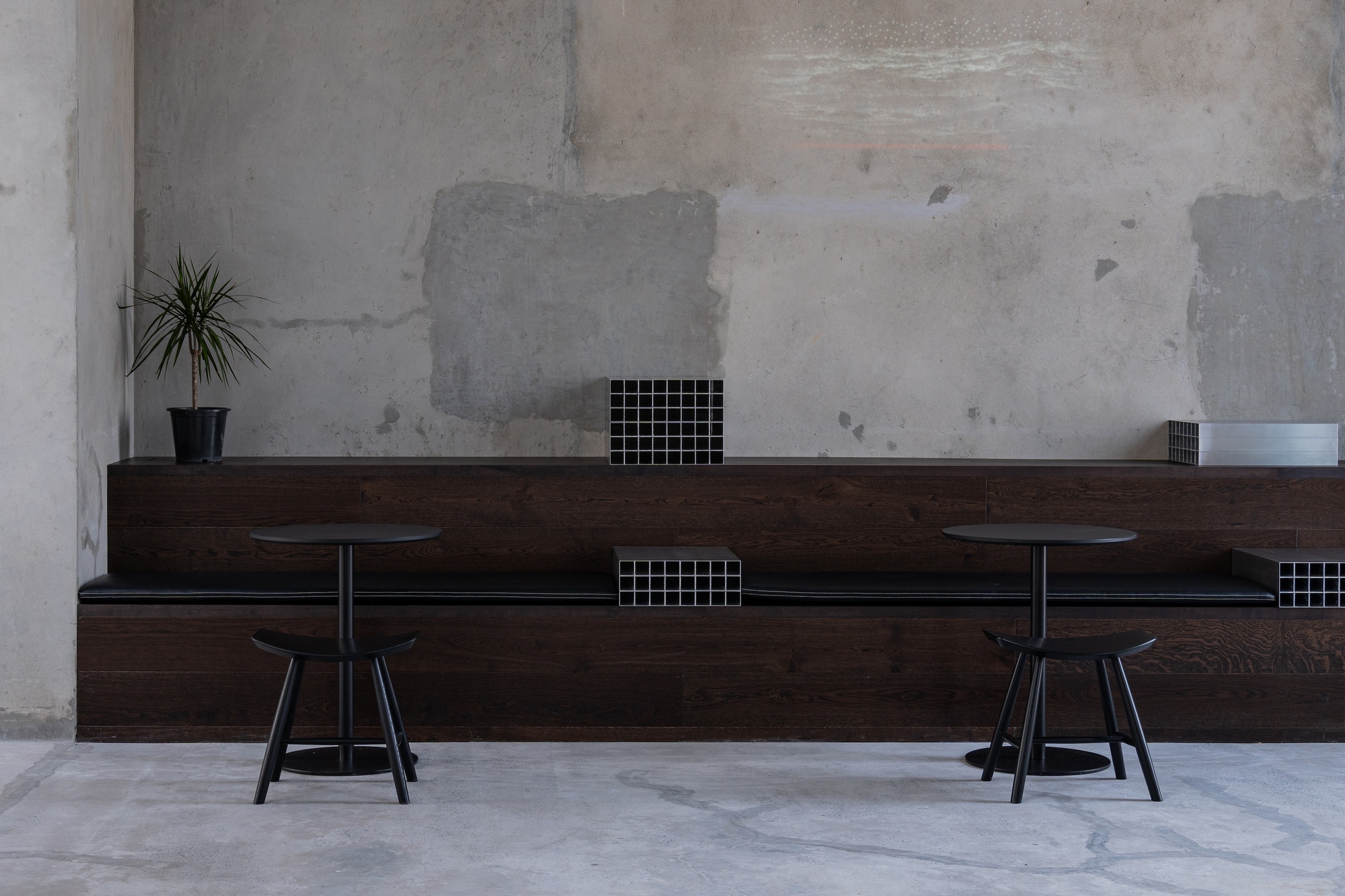 Dark timber bench seating with grid ventilation openings against a patched concrete wall