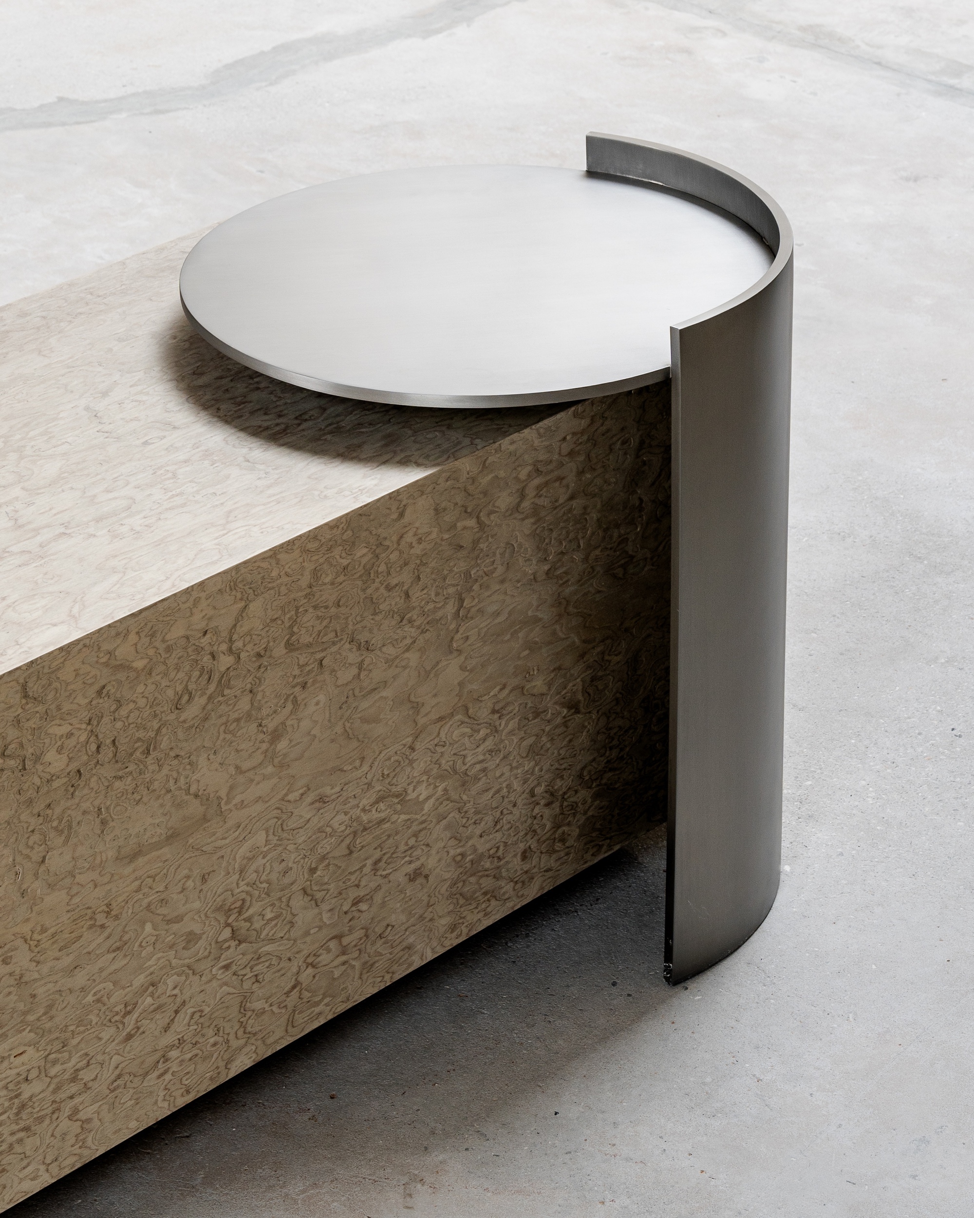 Detail of curved metal edge wrapping a circular table top above a concrete plinth