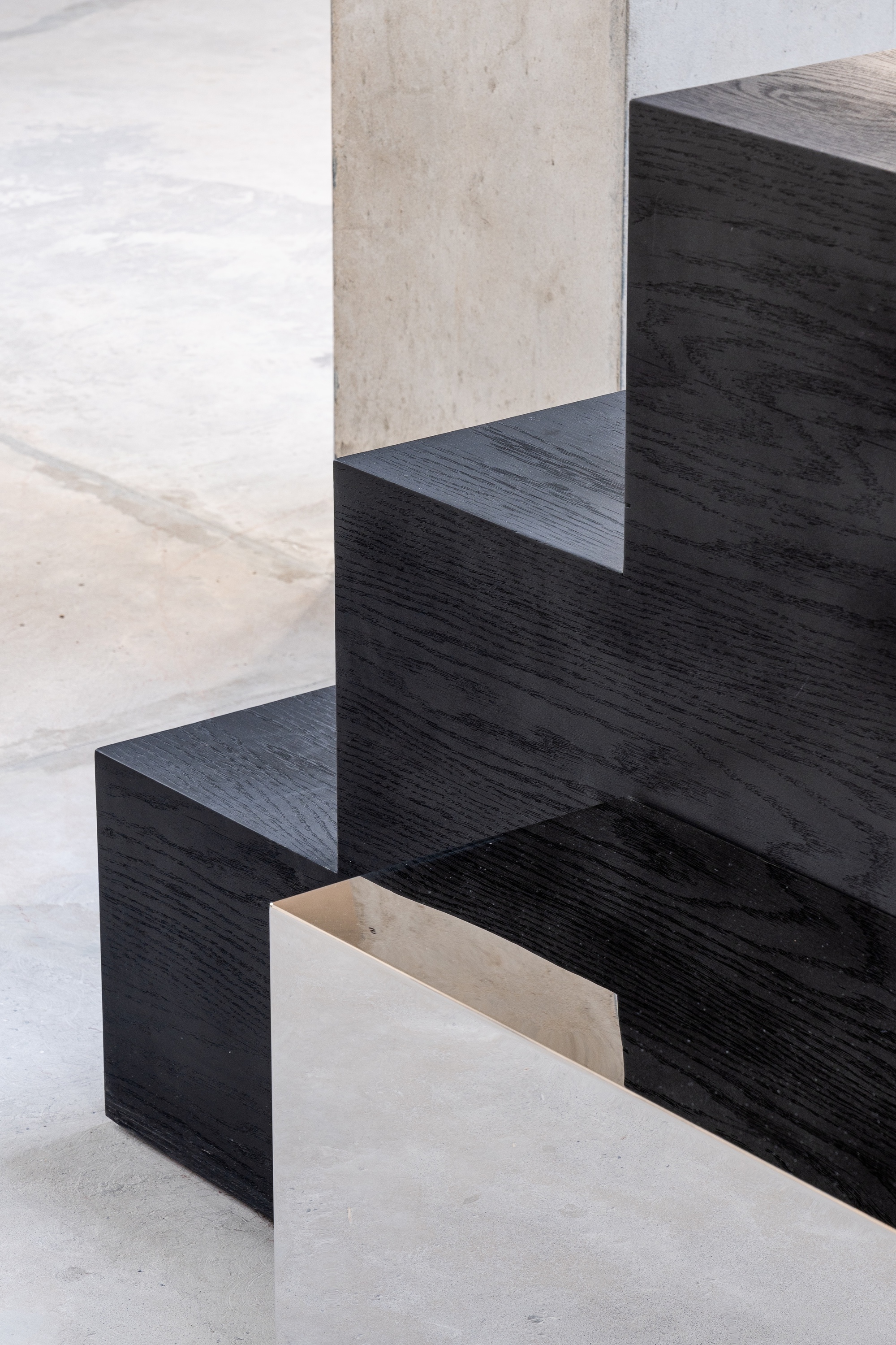 Blackened timber stair treads forming stepped seating beside a concrete column