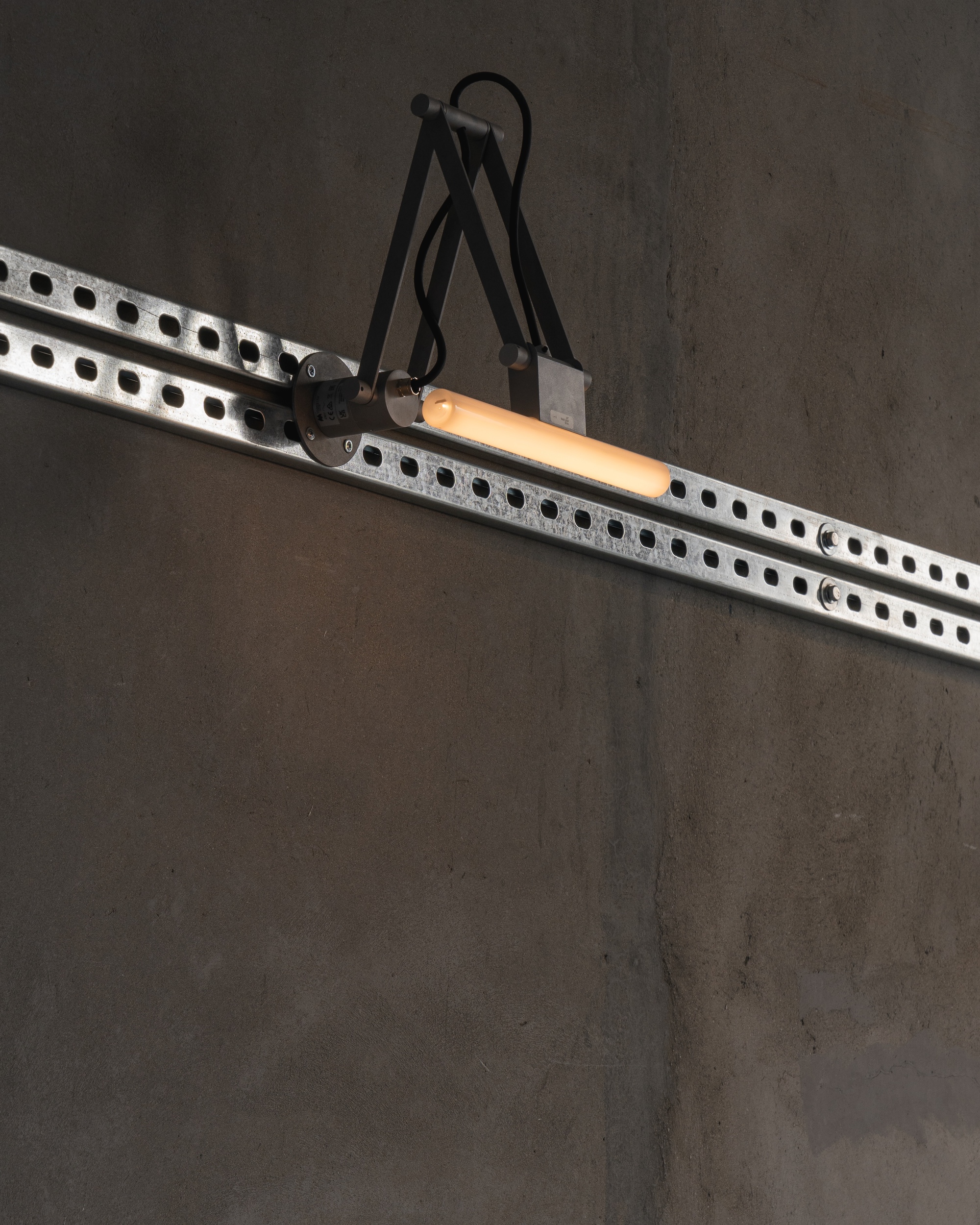 Articulated task light mounted on a perforated steel track against a grey wall