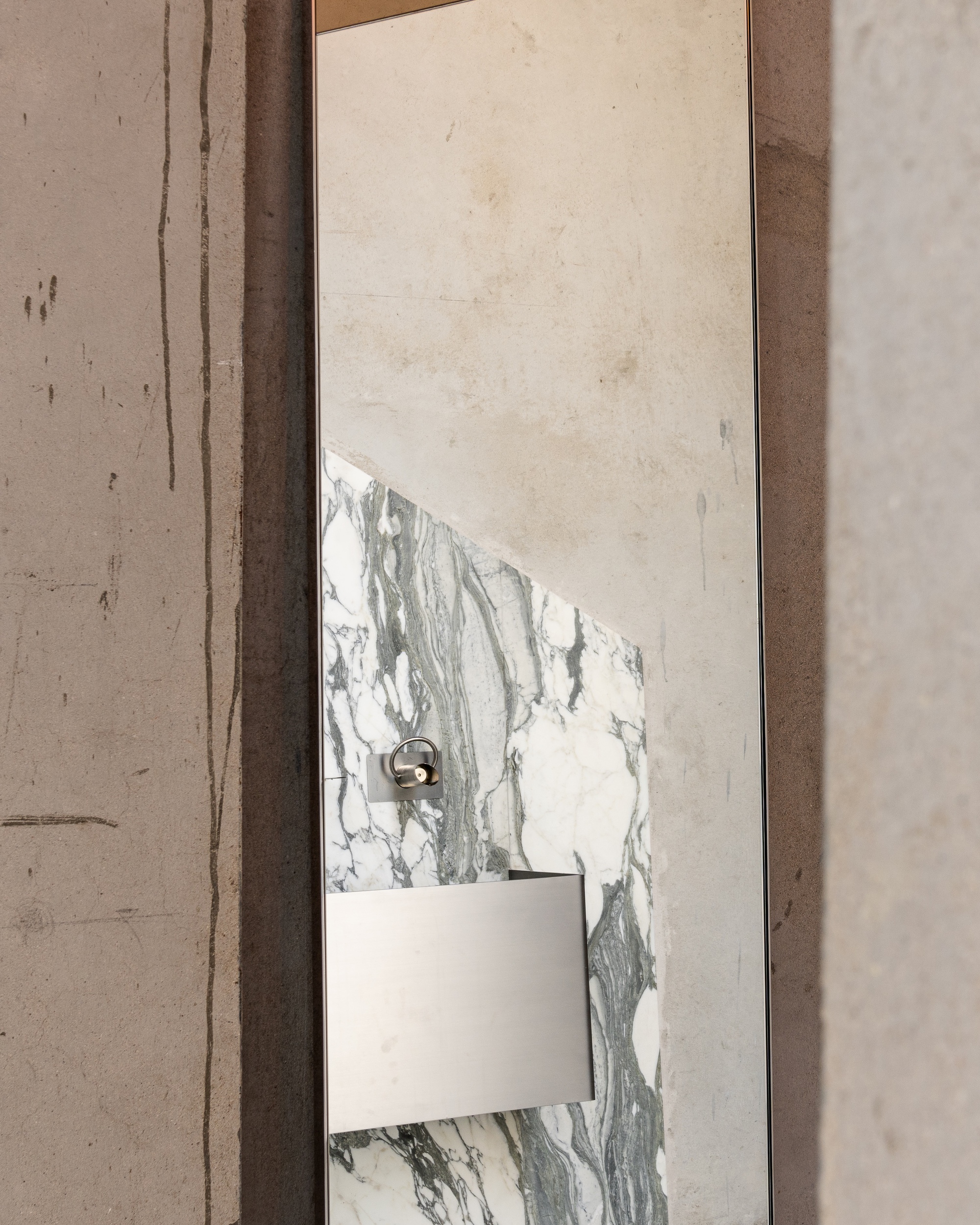 Detail of a marbled stone panel with white switch plate and bronze fixture against a plastered wall