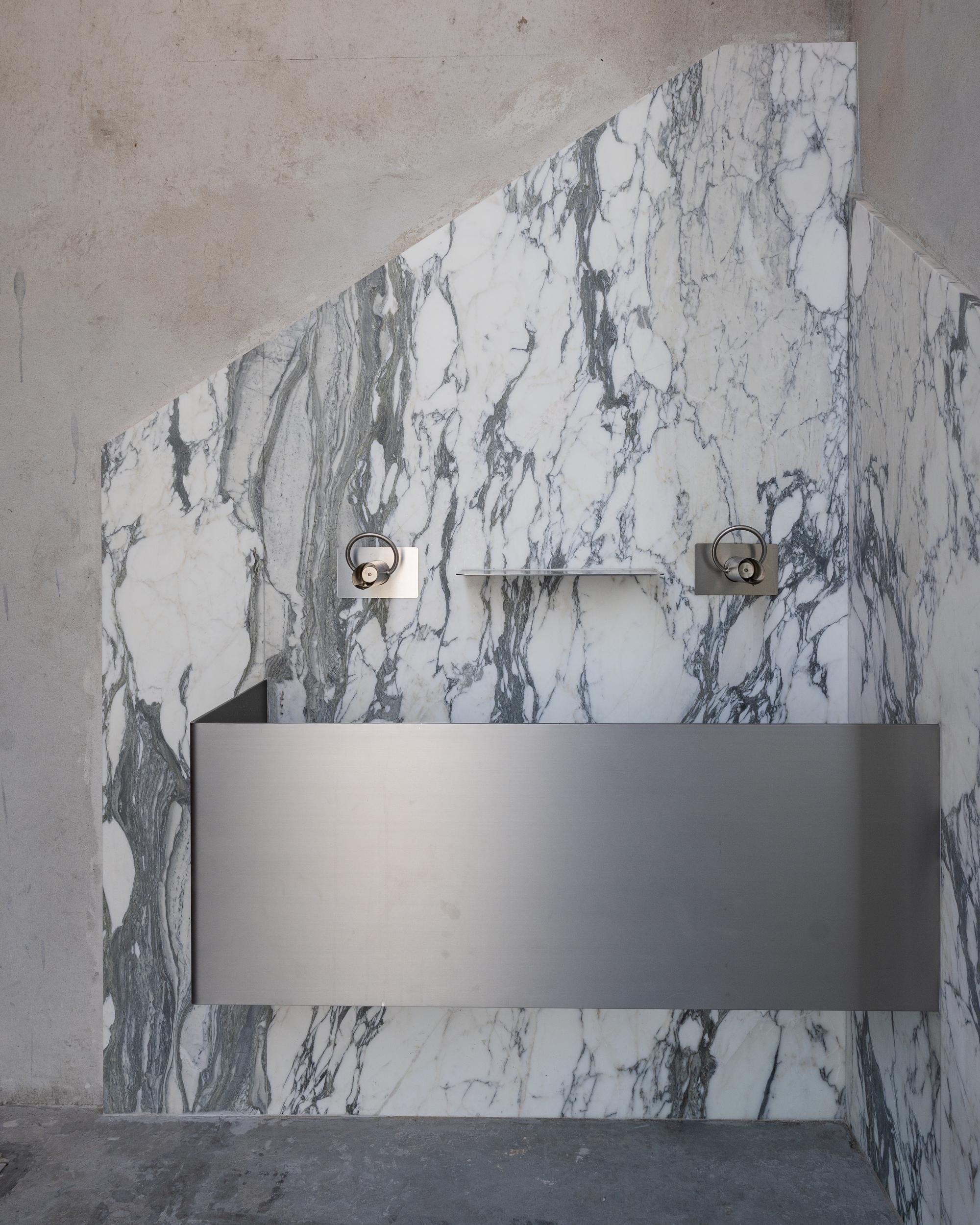 White marbled stone basin wall with exposed plumbing fixtures and a grey floating sink