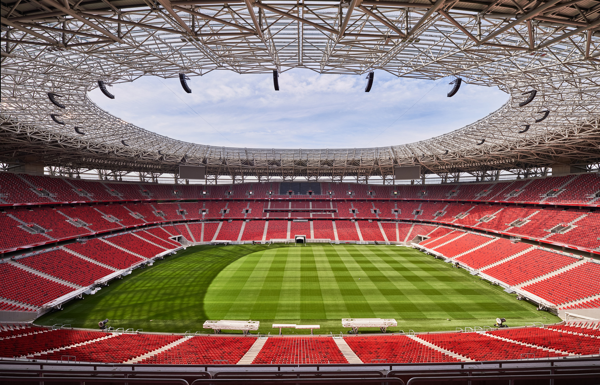 Interior view of the stadium bowl showing red seating tiers and the circular roof opening above the pitch