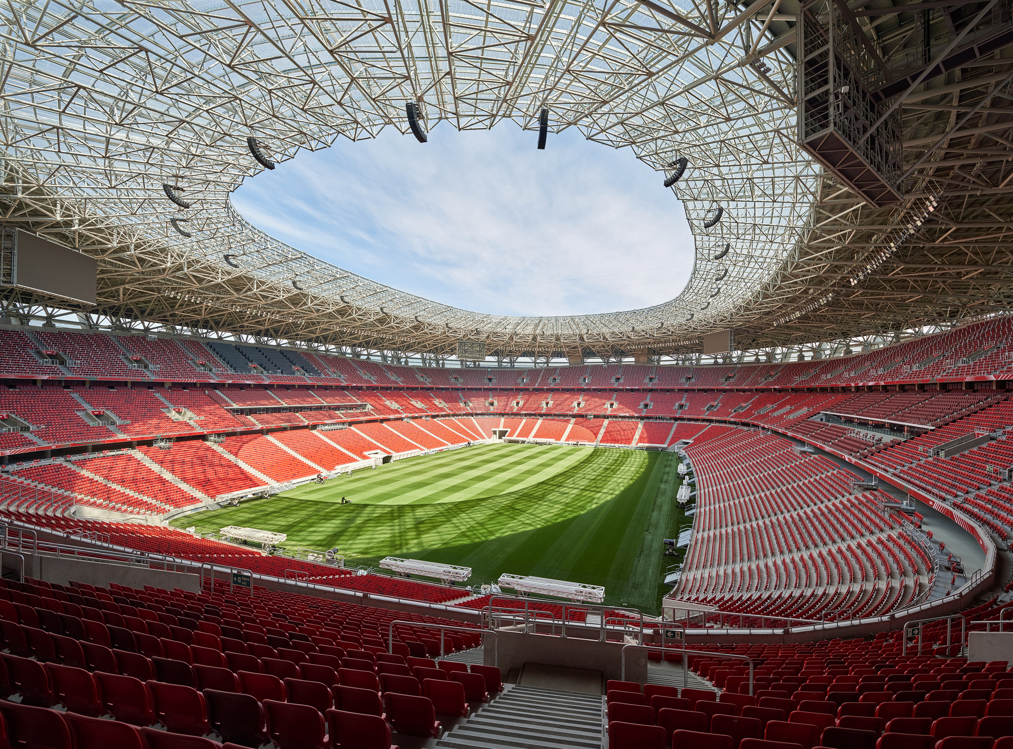 Stadium interior showing the oval roof oculus with exposed steel trusses above tiered red seating