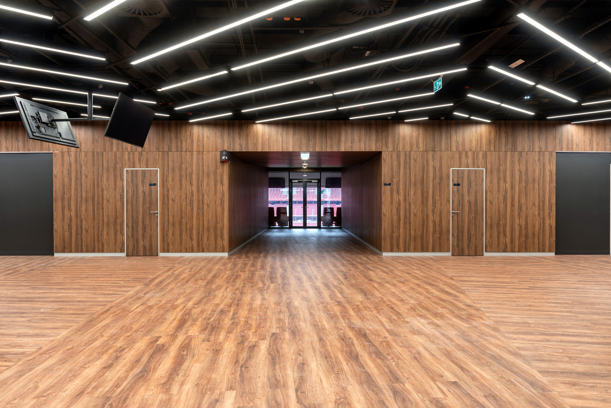 Corridor with timber paneled walls and wood flooring leading to glazed entrance doors under linear lighting