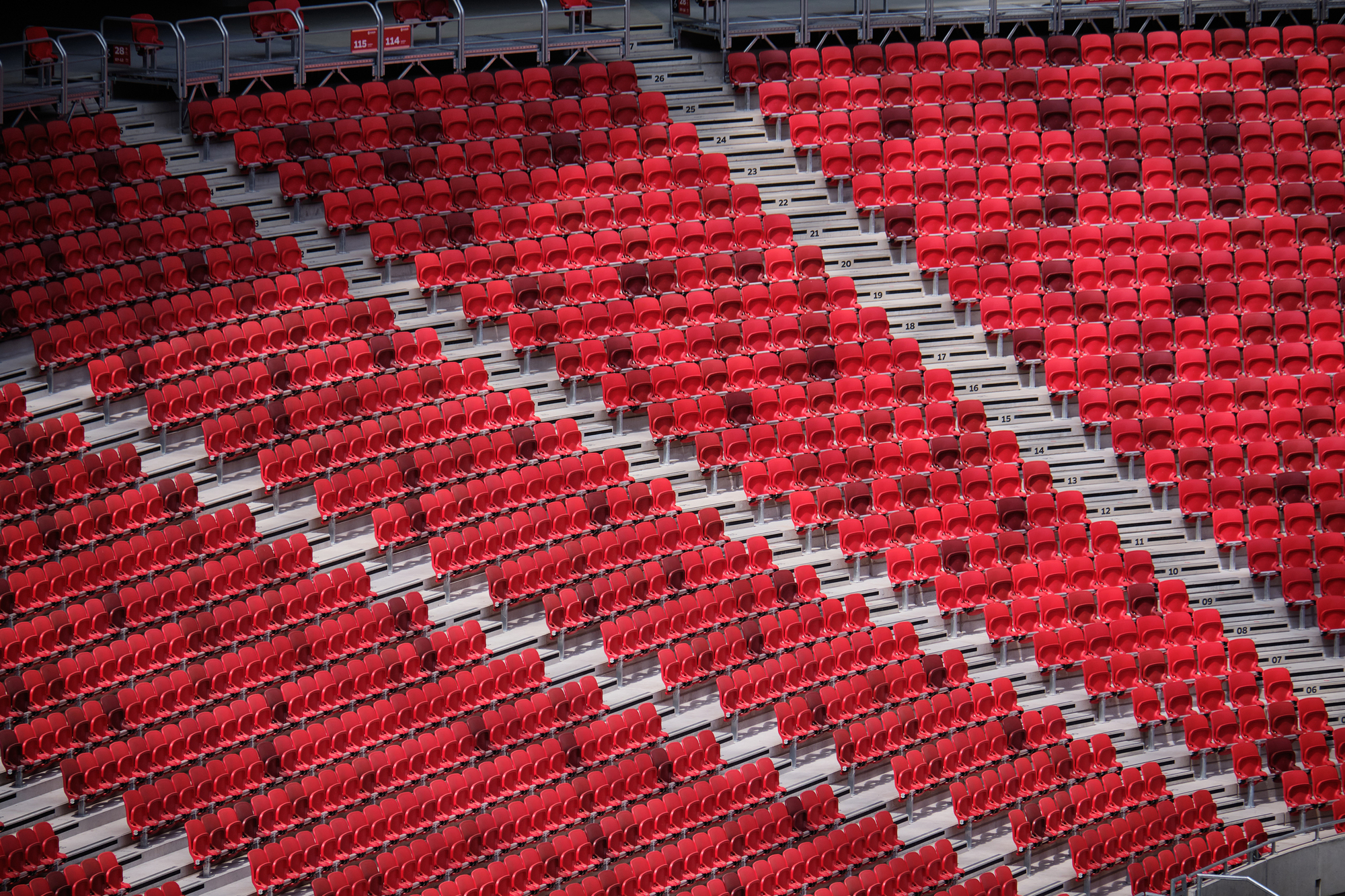 Diagonal view across stadium seating rows with red seats and grey concrete aisles
