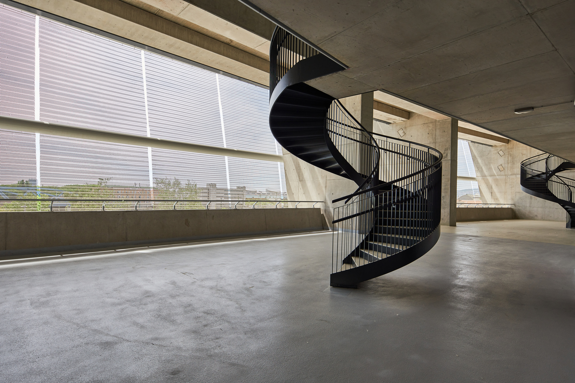 Black spiral staircase on a concrete floor with large horizontal windows overlooking a distant landscape