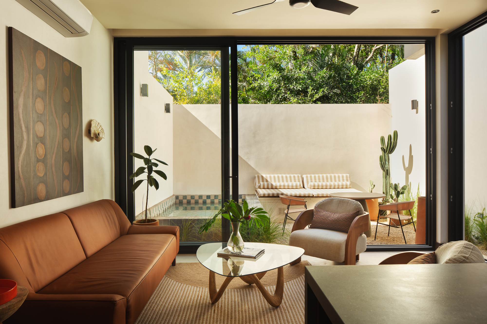 Living room opening to a walled terrace with tiled fountain and outdoor furniture beneath afternoon sun