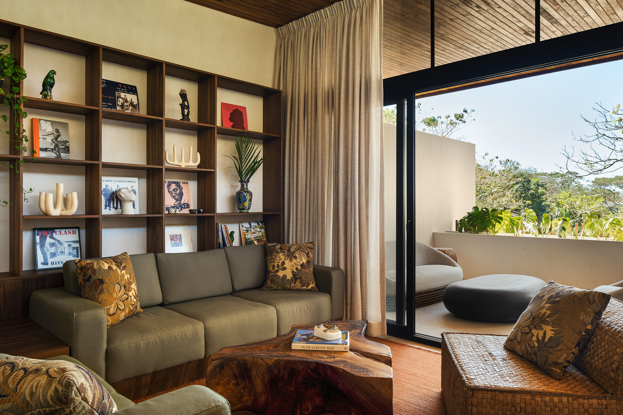 Interior lounge with timber bookshelves and slatted ceiling opening to a private terrace beyond glazed doors