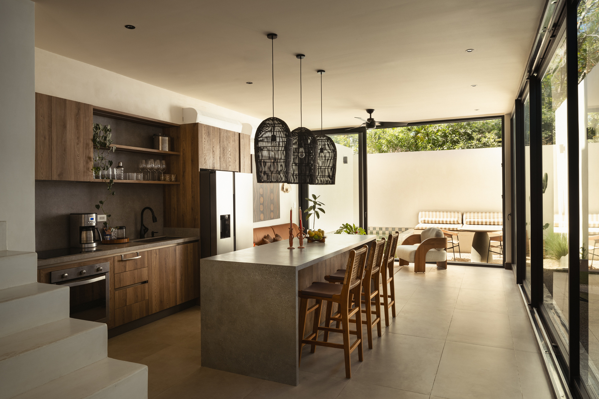 Open kitchen with concrete island, walnut cabinetry and sliding glass doors opening to a courtyard