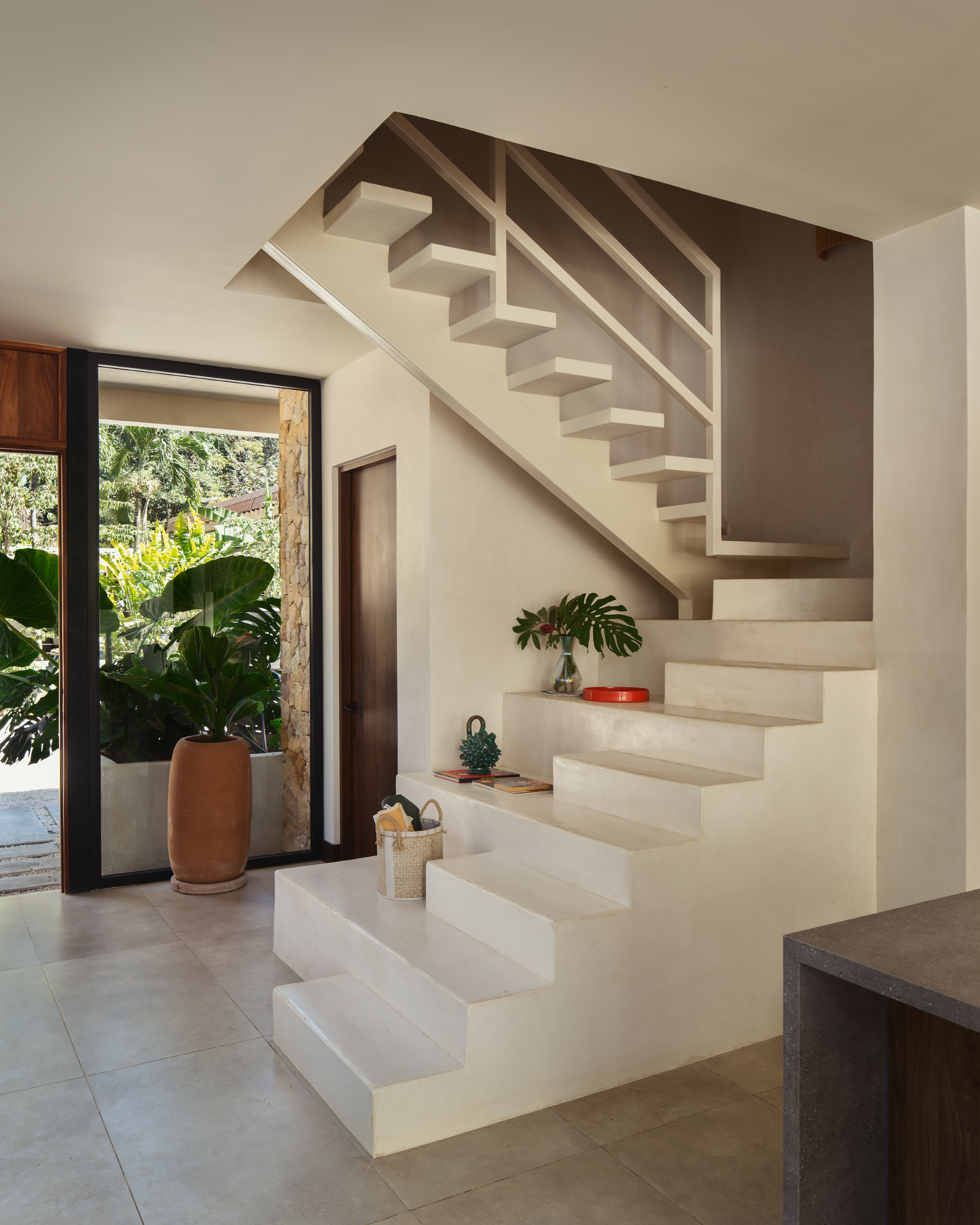 Pale plaster staircase ascending from entry hall with potted plant and view to garden