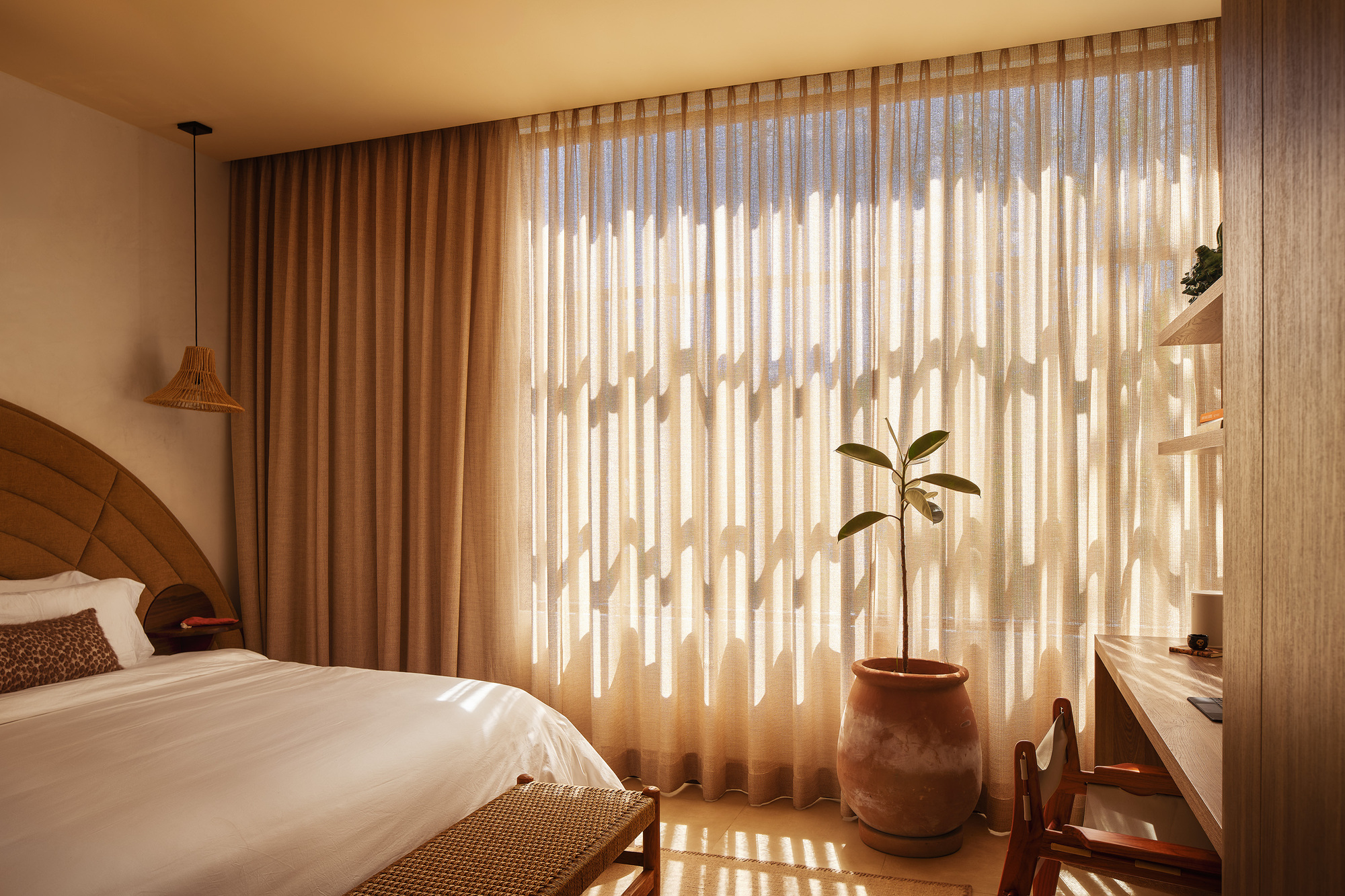 Bedroom with sheer curtains casting striped shadows from the vertical timber louvers beyond