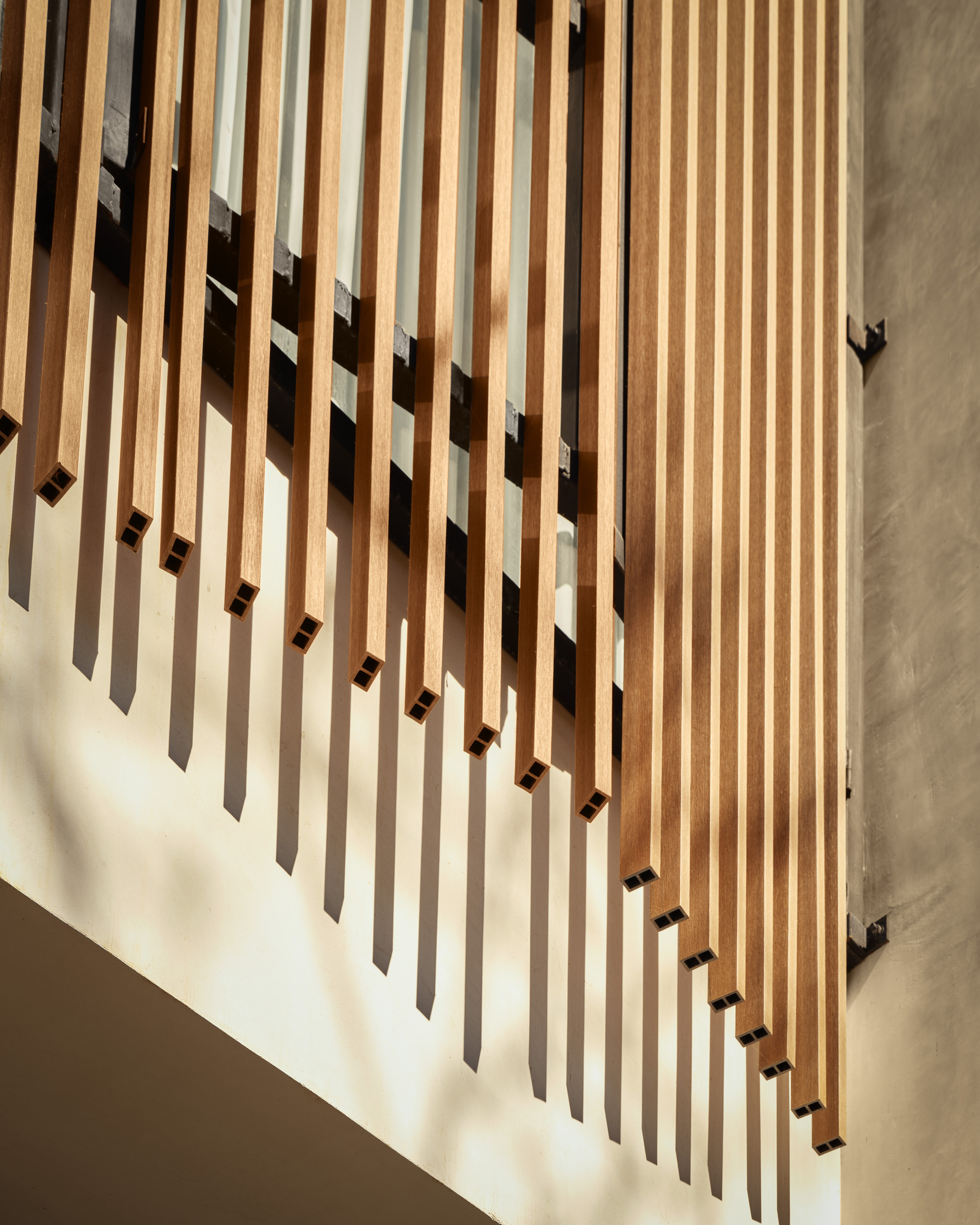Vertical timber slat screen with staggered shadows cast by afternoon sunlight on a white wall