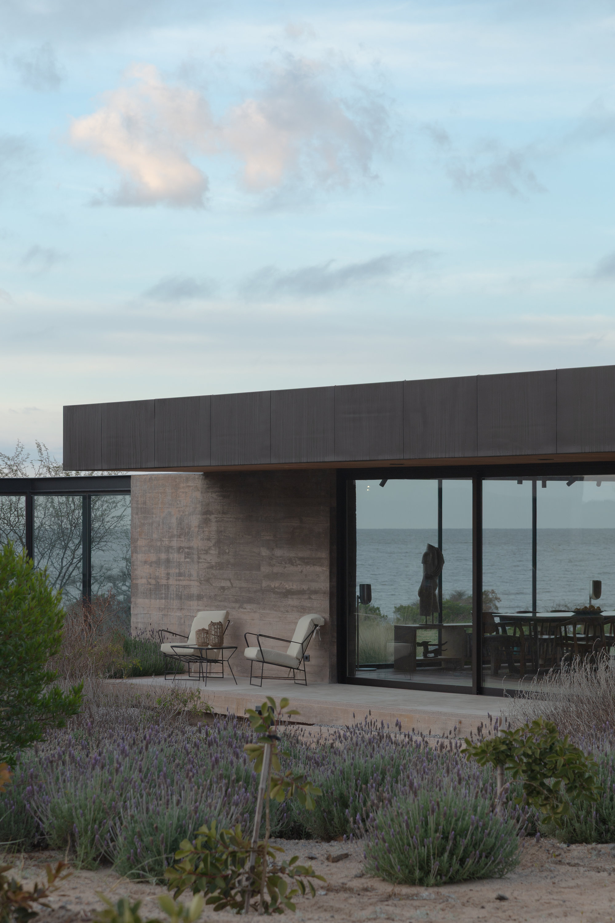 Covered patio with seating overlooking the ocean framed by native plantings at dusk