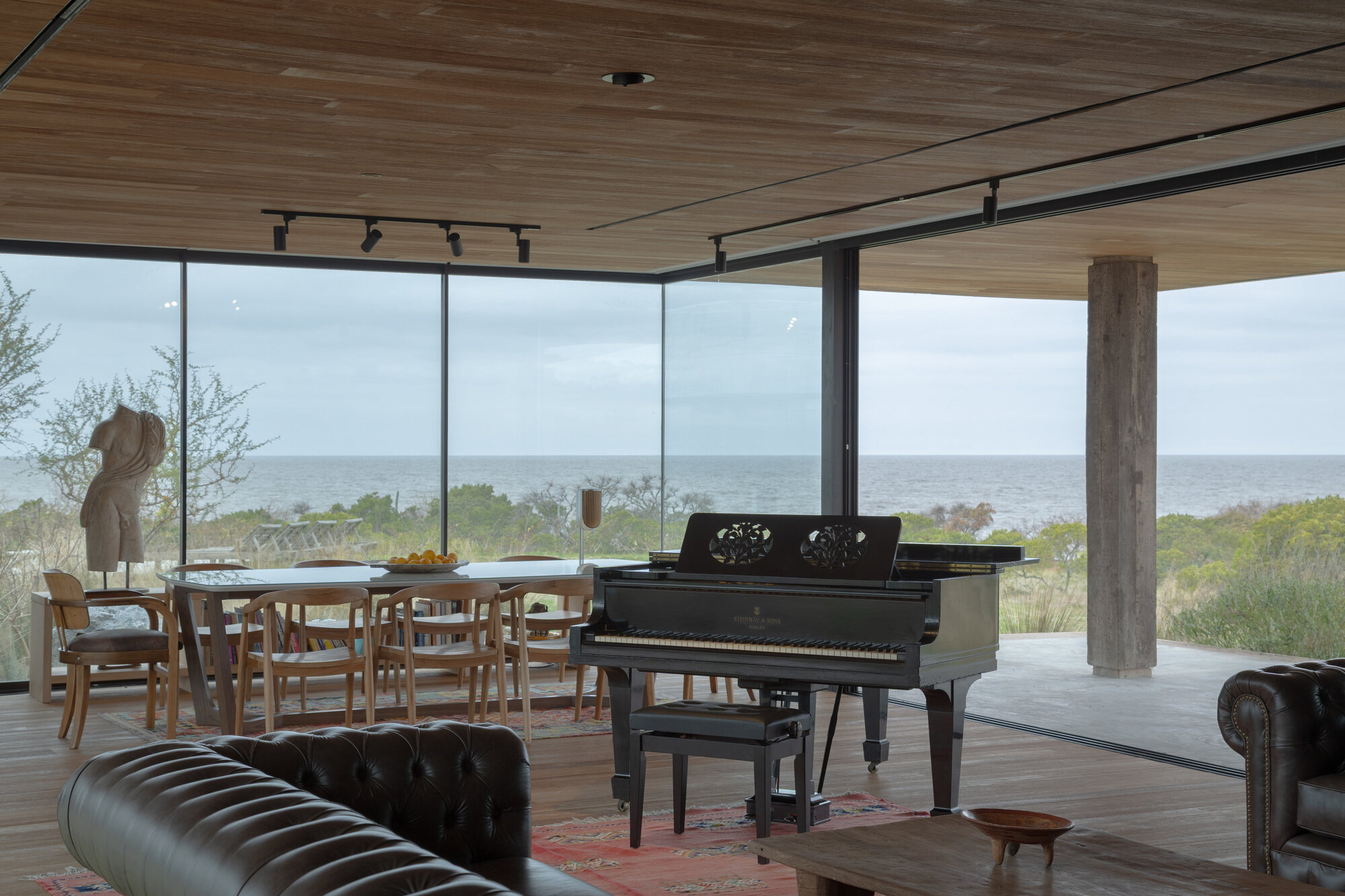 Dining and living area with glazed walls opening to the ocean horizon under diffused daylight