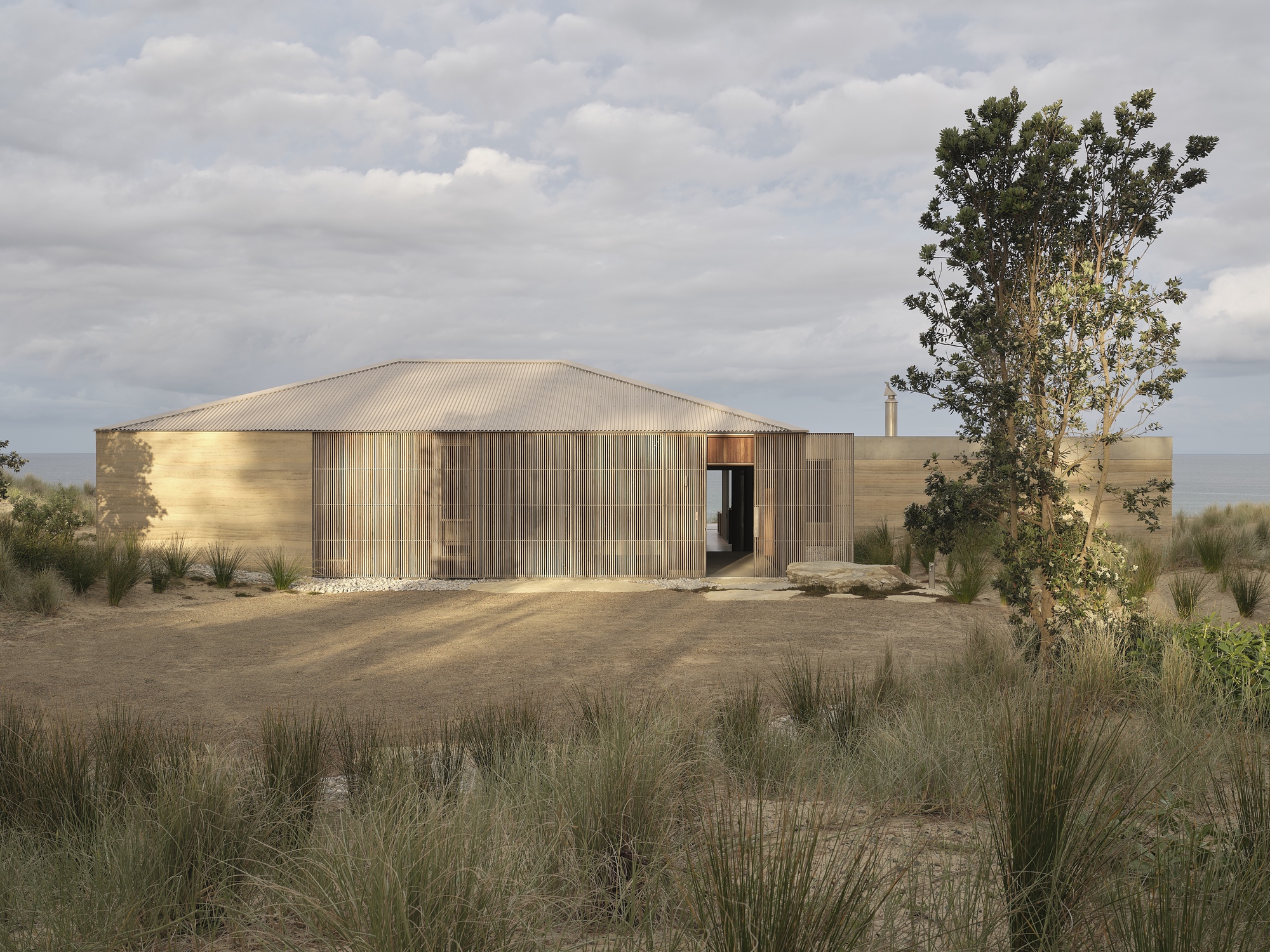 Timber-clad facade with curved metal roof set among native grasses under cloudy afternoon skies