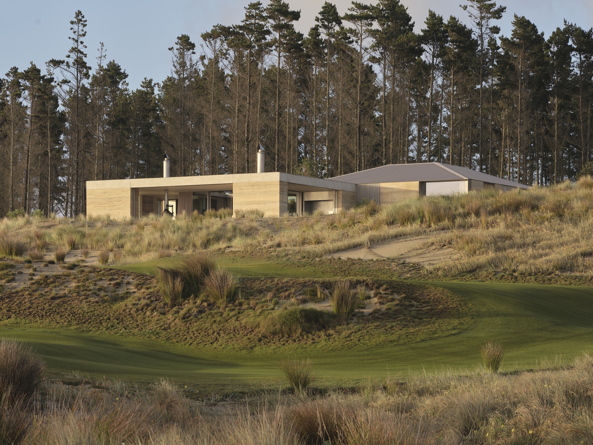 Low-slung pavilions with flat and gabled roofs positioned on a hillside overlooking a fairway