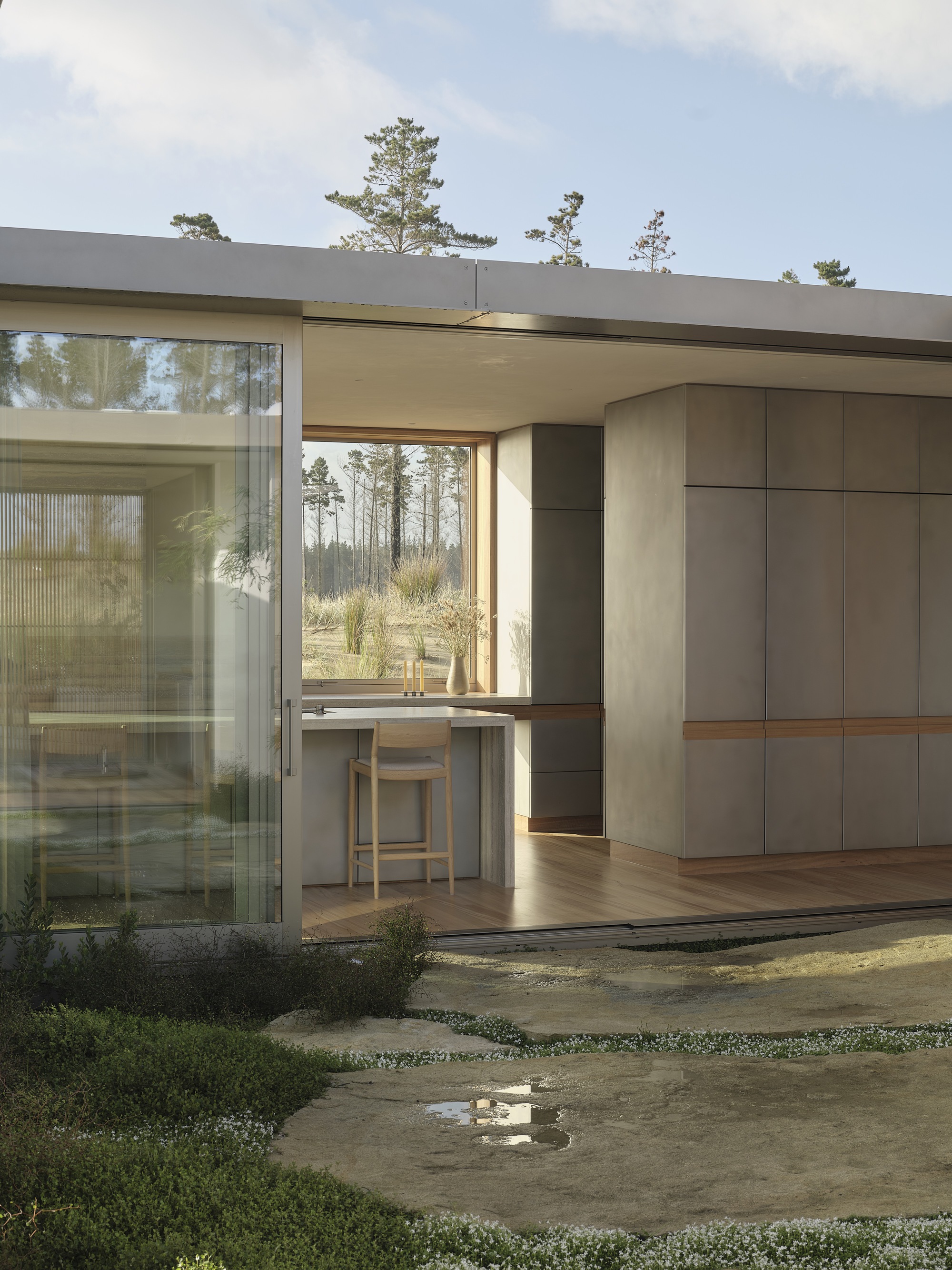 Open corner of the living space showing timber cabinetry and barstool framed by courtyard plantings