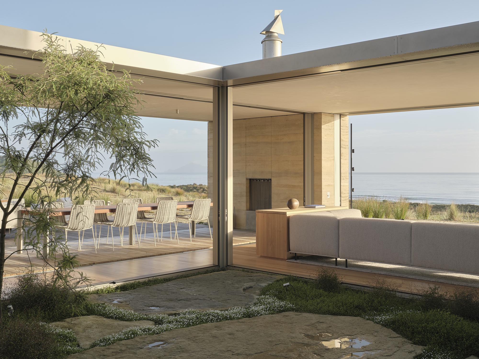 View through sliding glass doors to timber deck and outdoor seating area overlooking coastal landscape