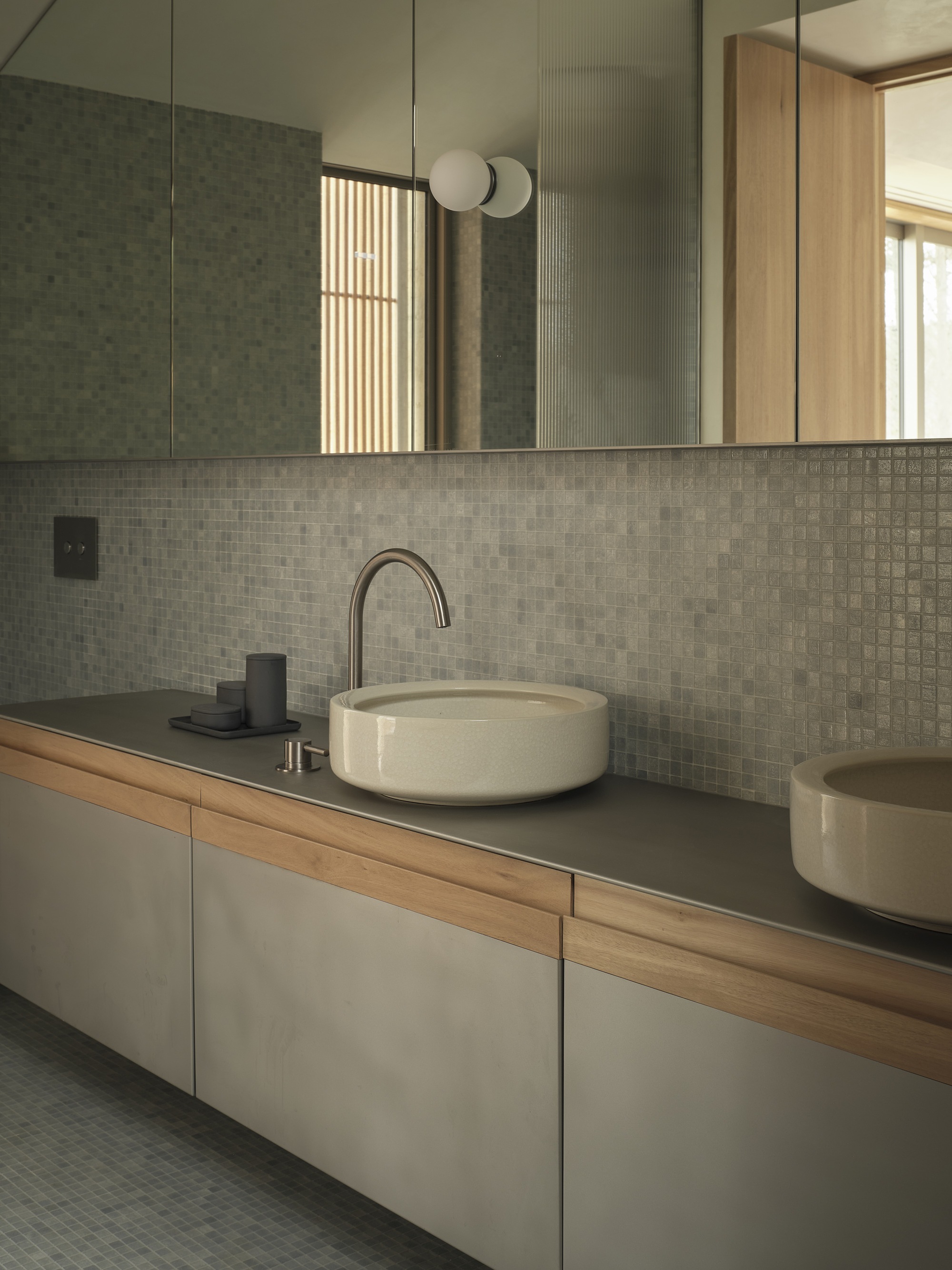 Double vanity with circular stone basins on dark countertop beneath gridded tile backsplash and mirror
