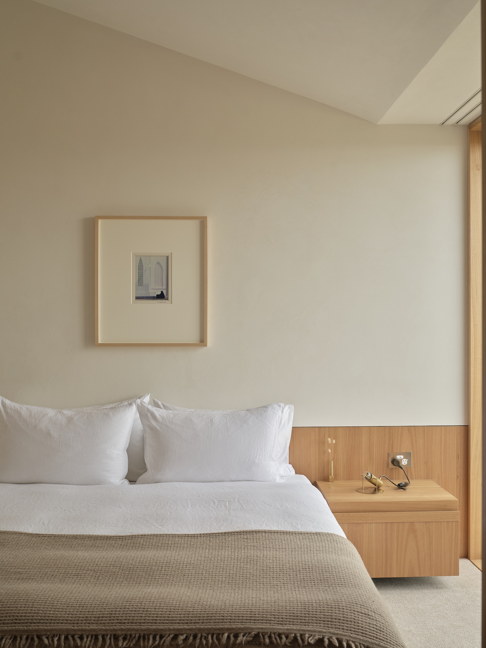 Bedroom with integrated timber bedside shelf and framed artwork on pale plaster wall