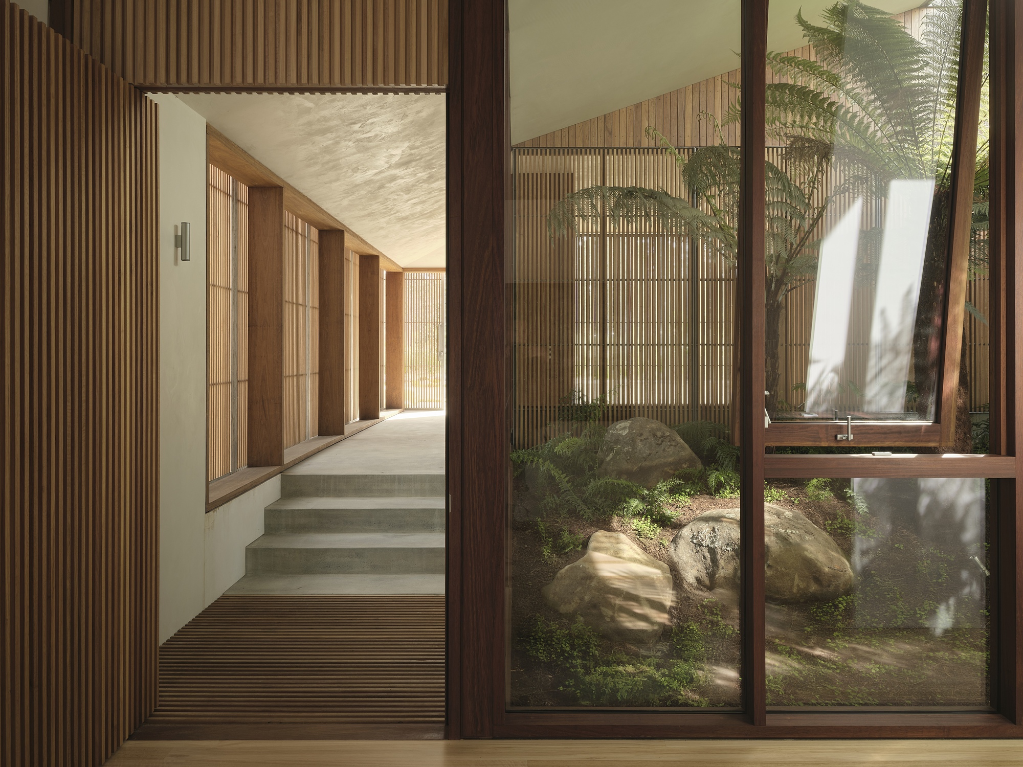 View through glass doors to a timber-lined corridor with steps and a small rock garden