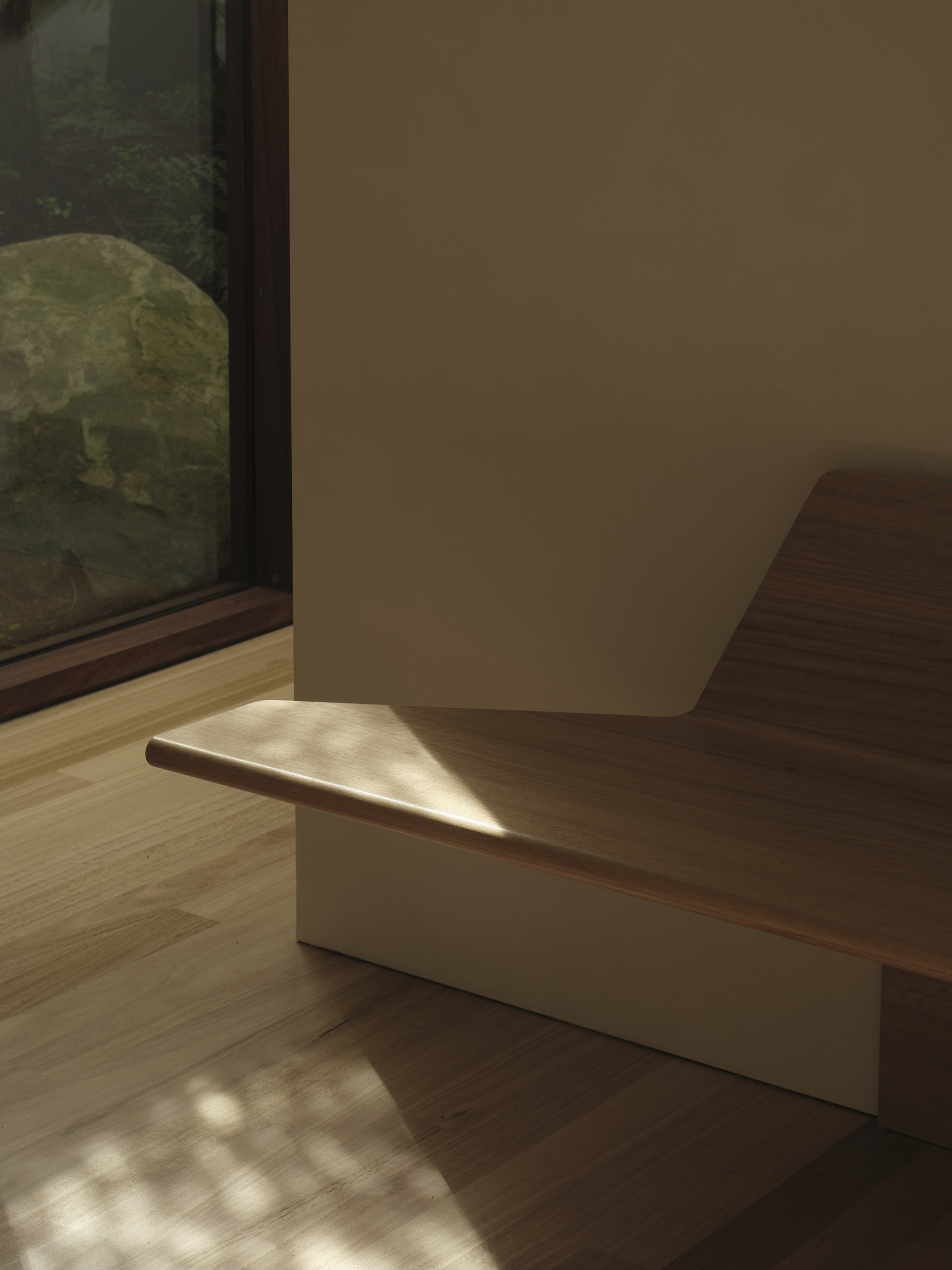 Built-in timber bench with cream plinth beside a floor-to-ceiling window in dappled afternoon light