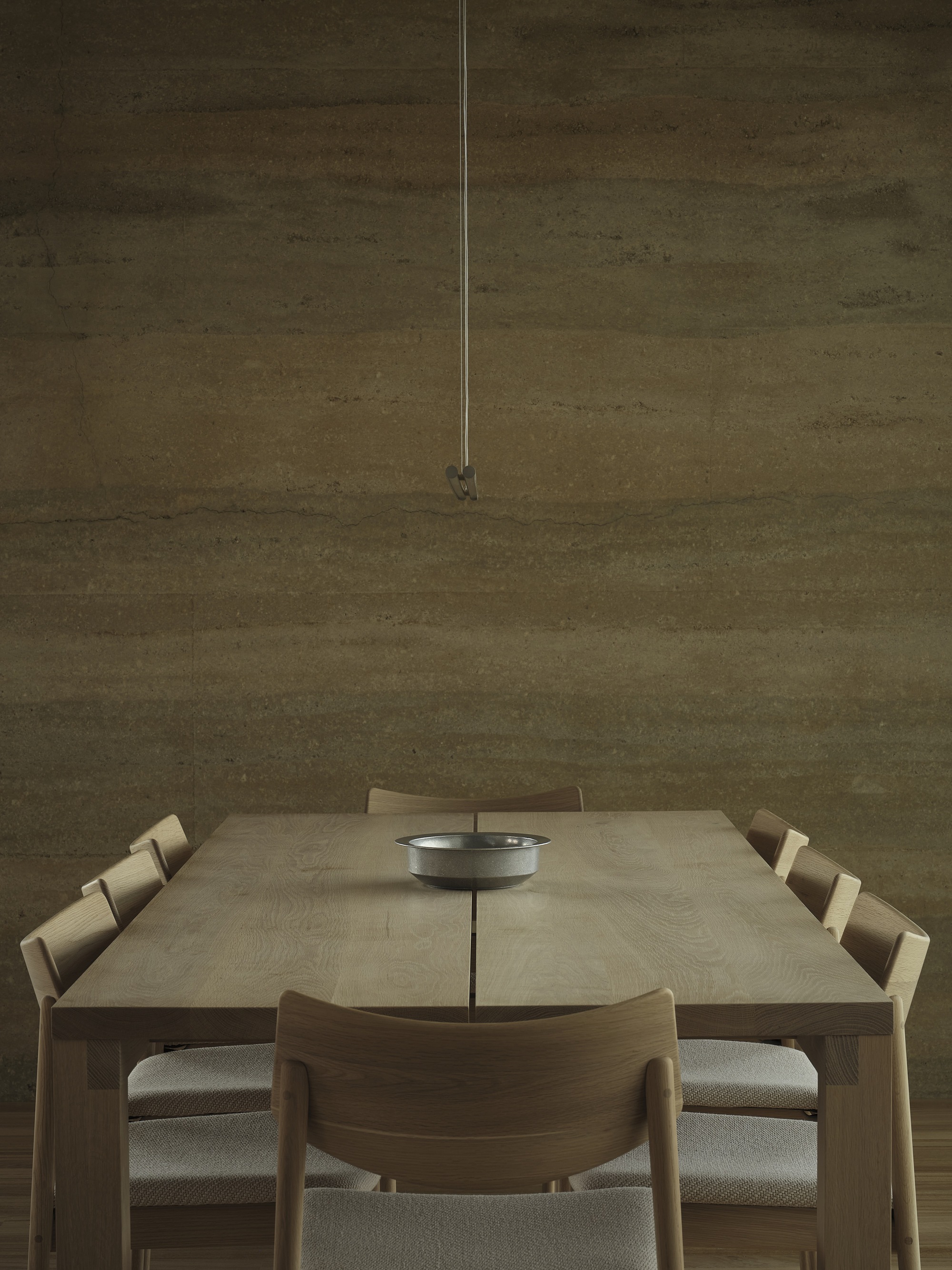Dining table with timber chairs and pendant light against a rammed earth wall