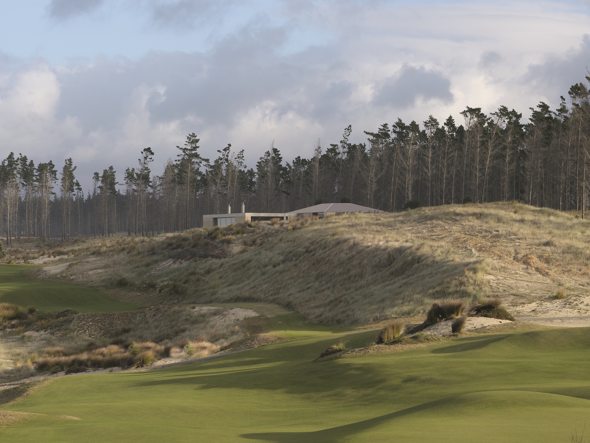 Low horizontal structure on a hillside overlooking a golf course with pine forest beyond