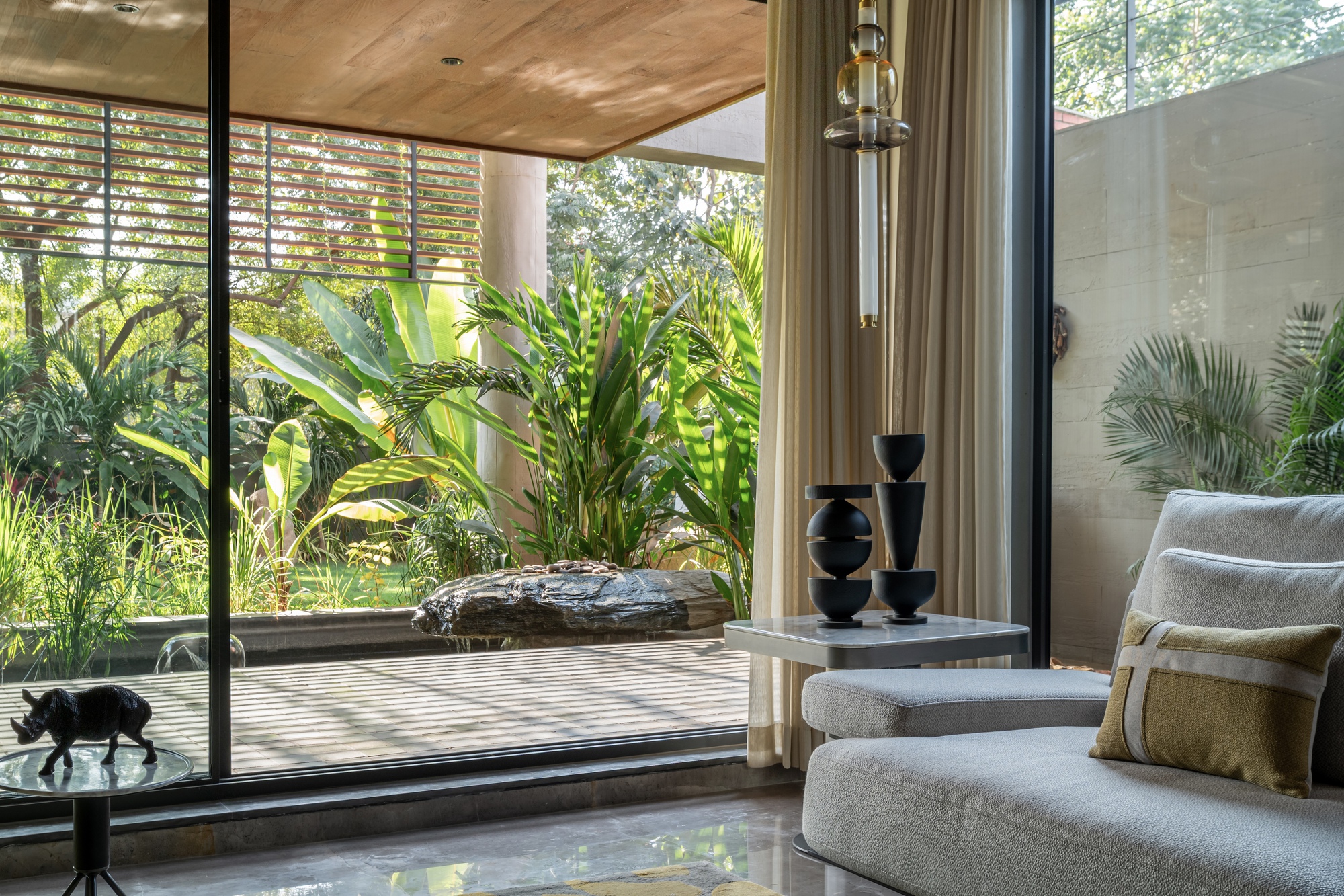 Interior living space opening to timber deck, water feature and lush garden through floor-to-ceiling glazing