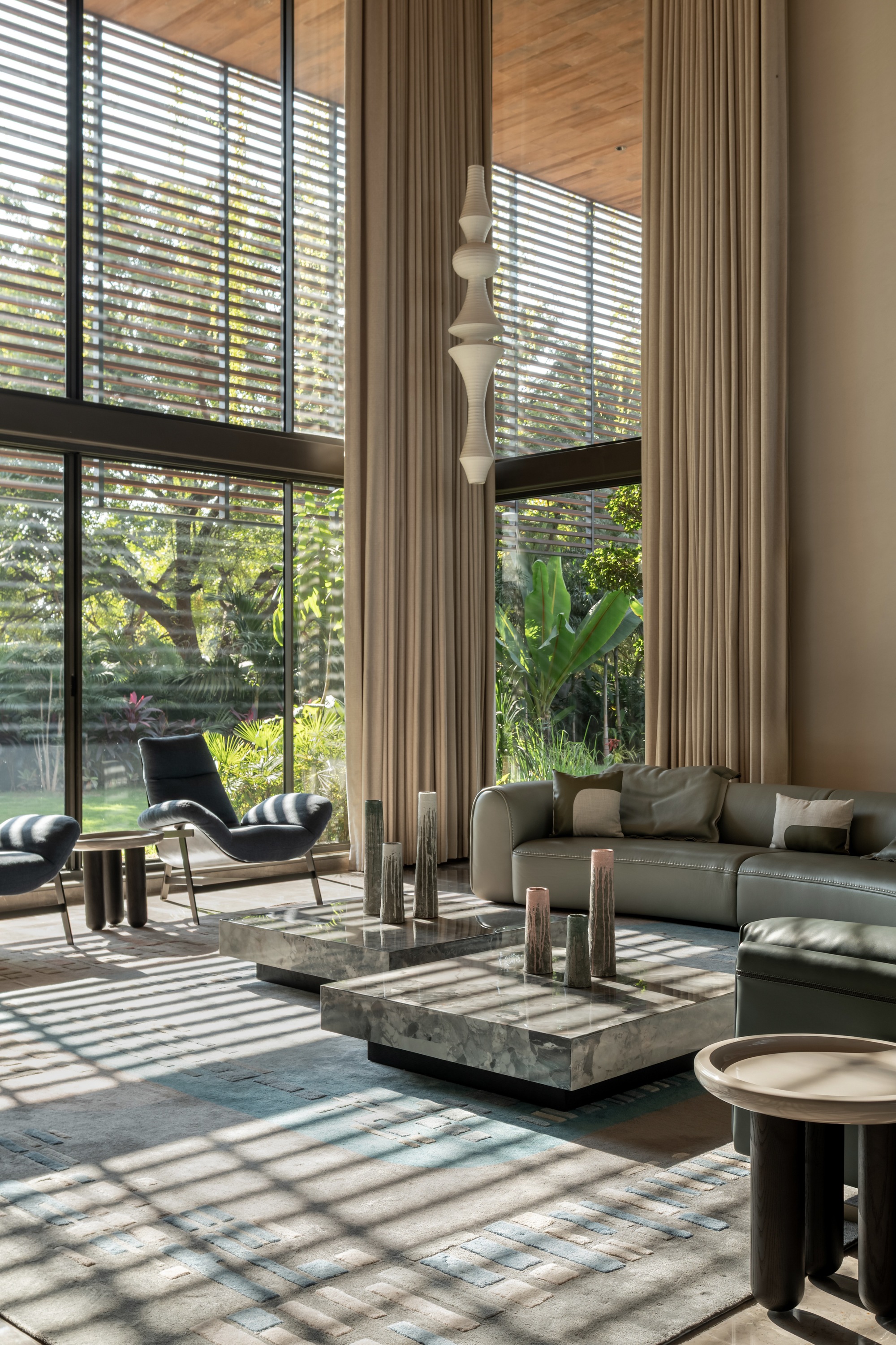 Double-height living room with horizontal louvered windows casting striped shadows across polished floor