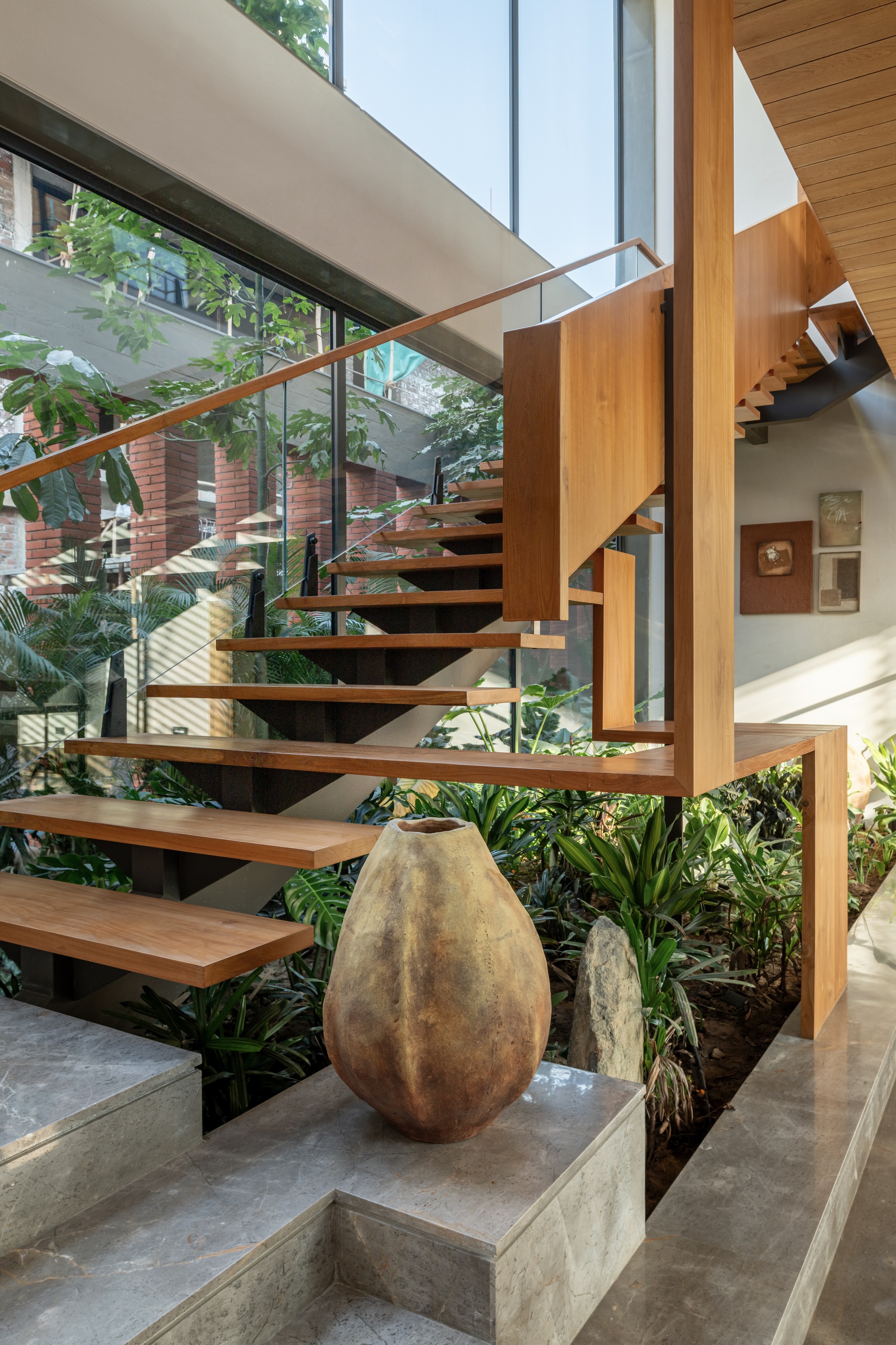 Cantilevered timber staircase with open risers ascending beside a planted interior courtyard