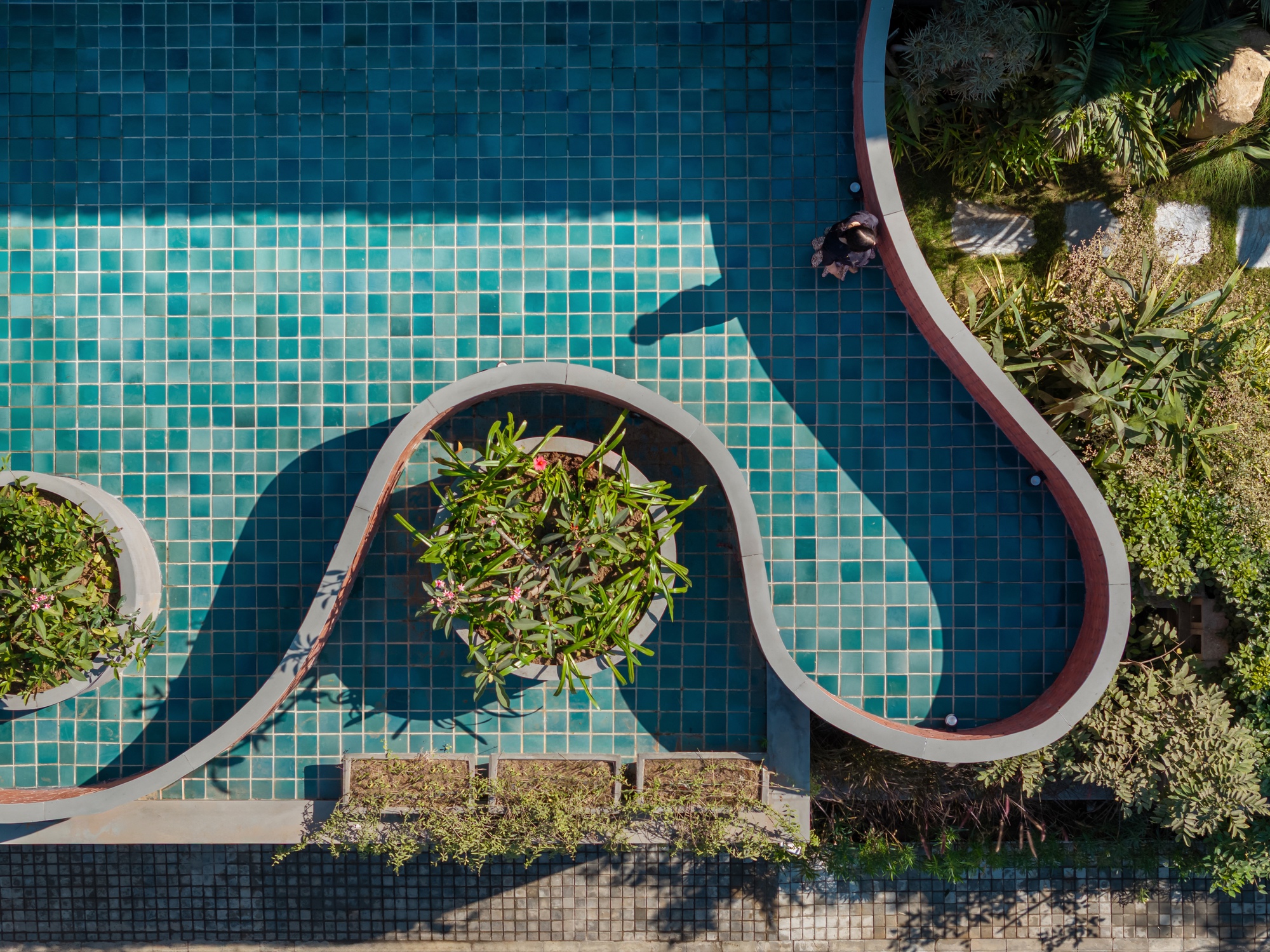 Aerial view of the turquoise mosaic tile pool with curving brick planters and tropical vegetation