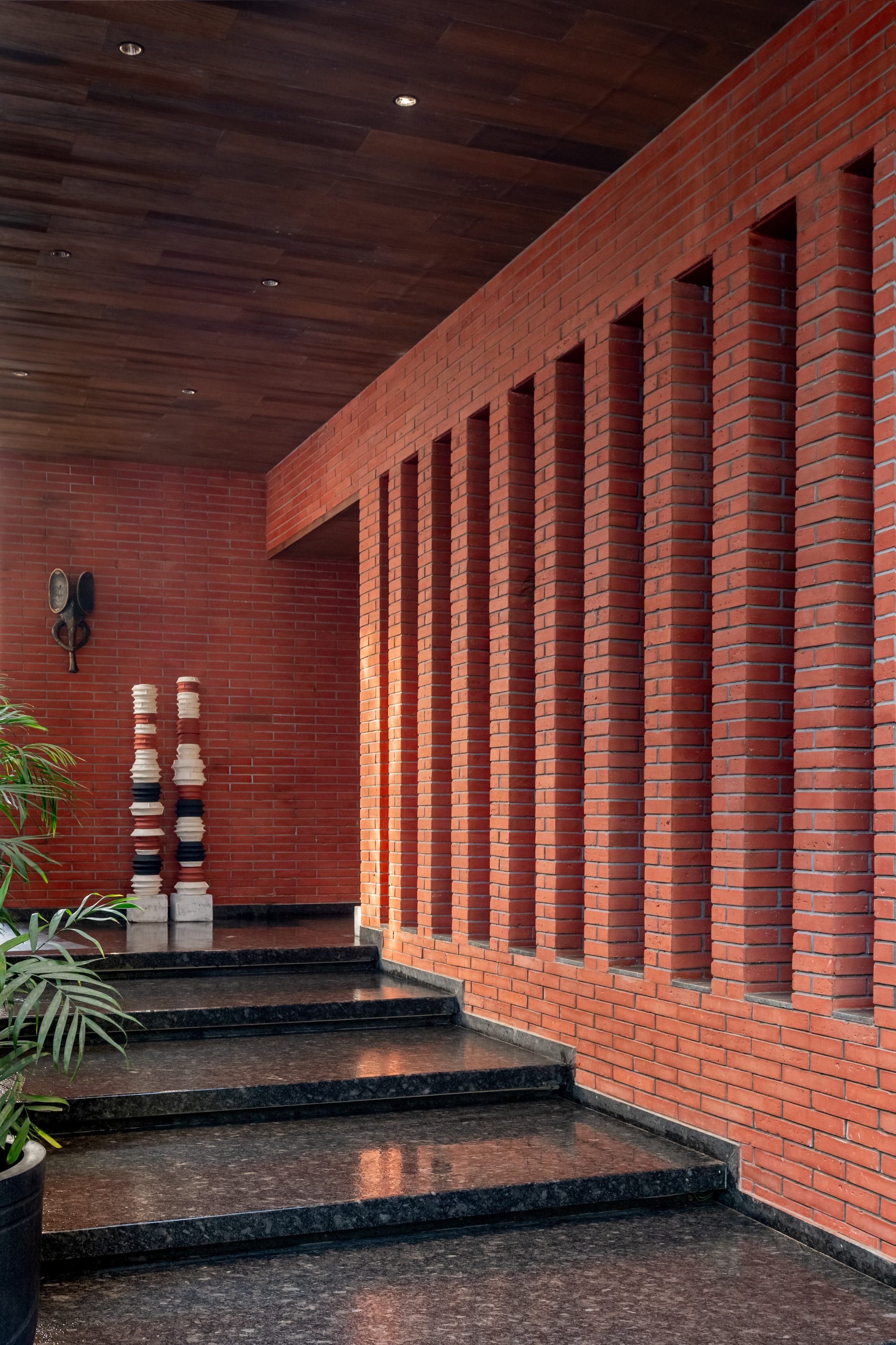 Interior staircase with terrazzo treads rising past a red brick wall with vertical recessed channels