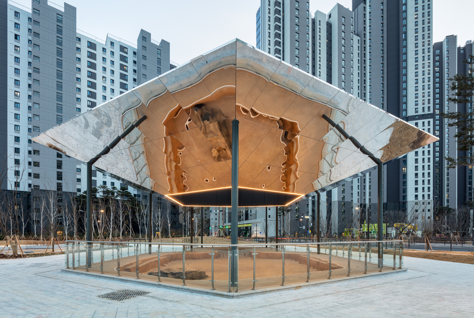 Faceted canopy suspended on steel columns with copper ceiling reflected in the circular glass enclosure below