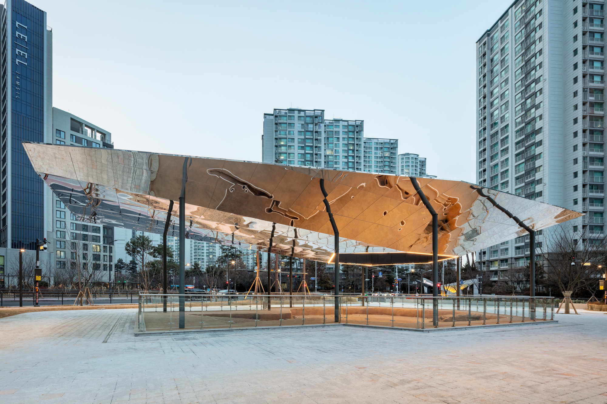 Timber canopy with angular cutouts supported by slender columns in an urban plaza at dusk