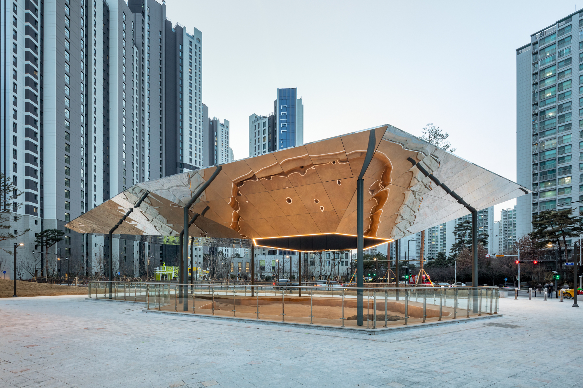 Illuminated underside of the fractured timber canopy with glass balustrade enclosing the plaza below
