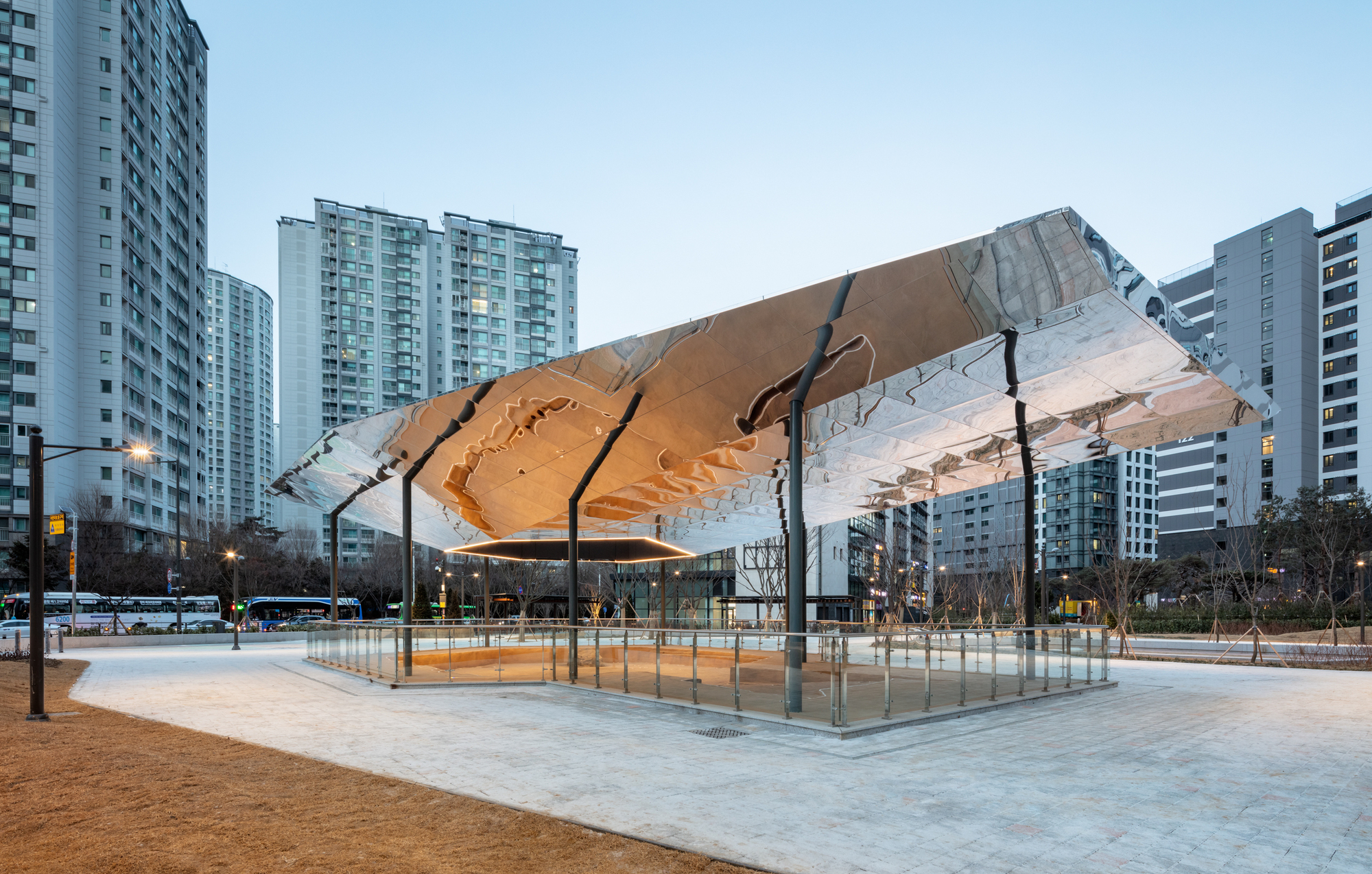 Angled view of the folded timber canopy structure framed by residential towers at twilight