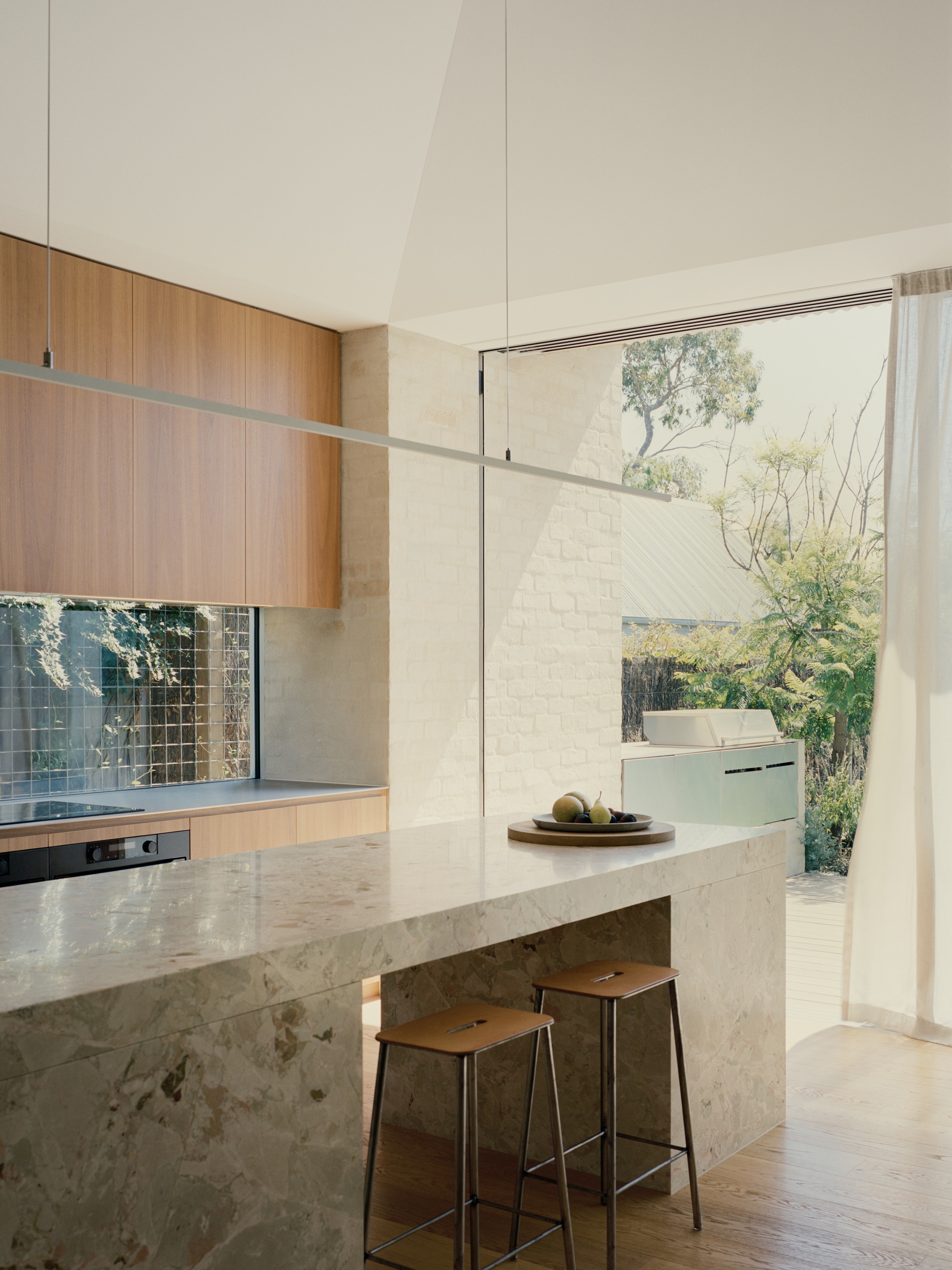 Kitchen island in mottled stone with timber cabinetry and glass doors opening to courtyard