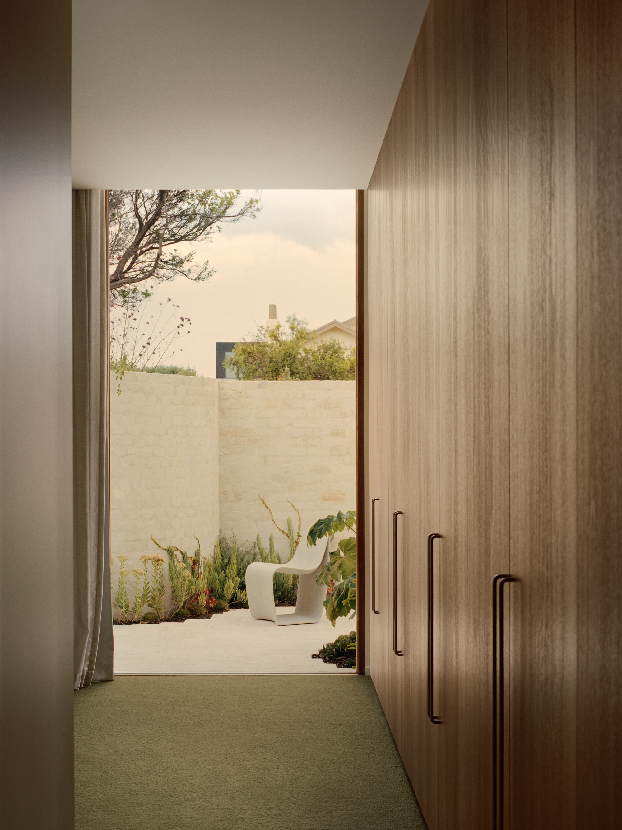 Hallway with timber joinery leading to planted courtyard with limestone walls
