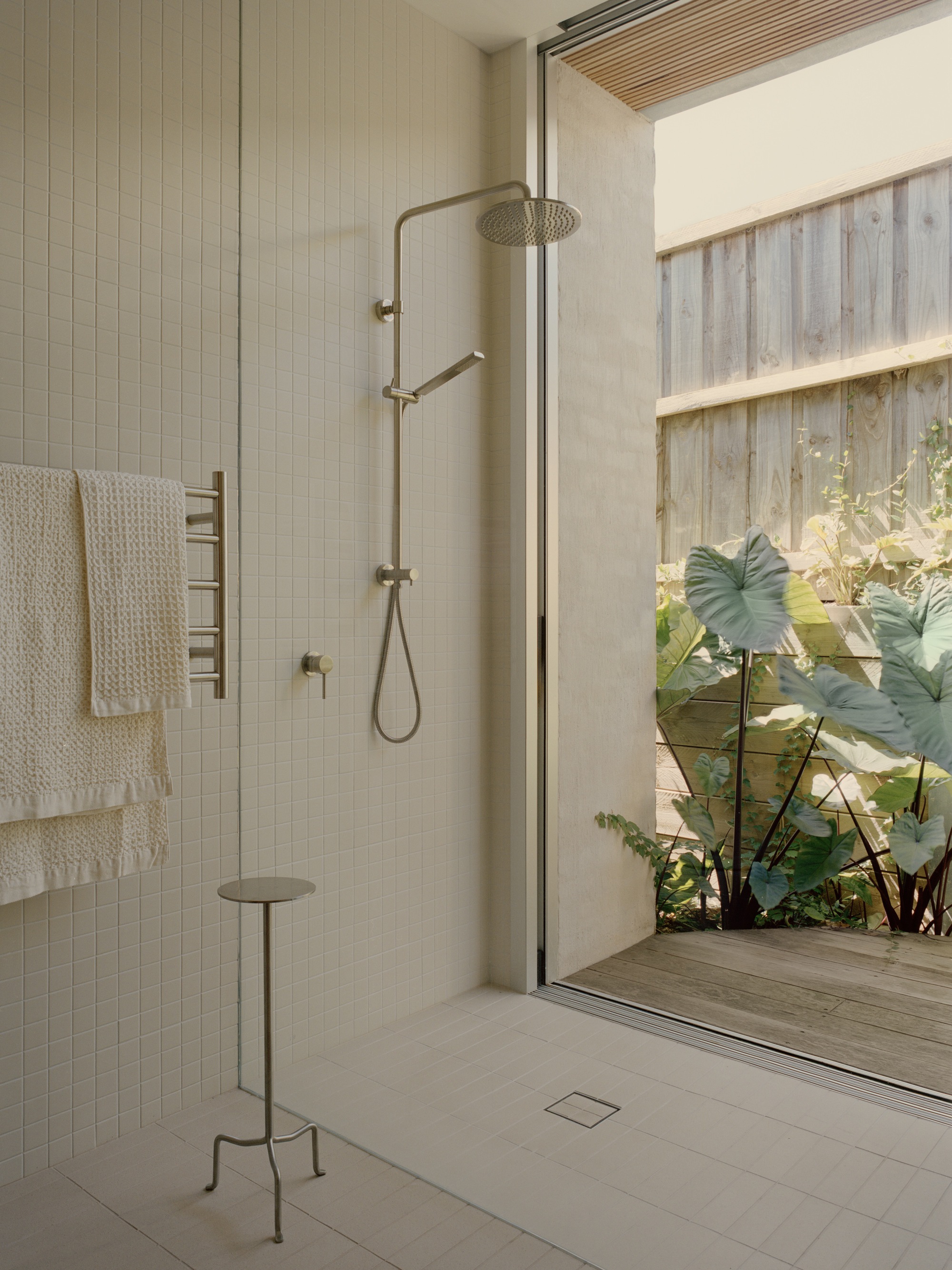 Walk-in shower with brass fixtures opening onto a private garden courtyard through sliding glass doors