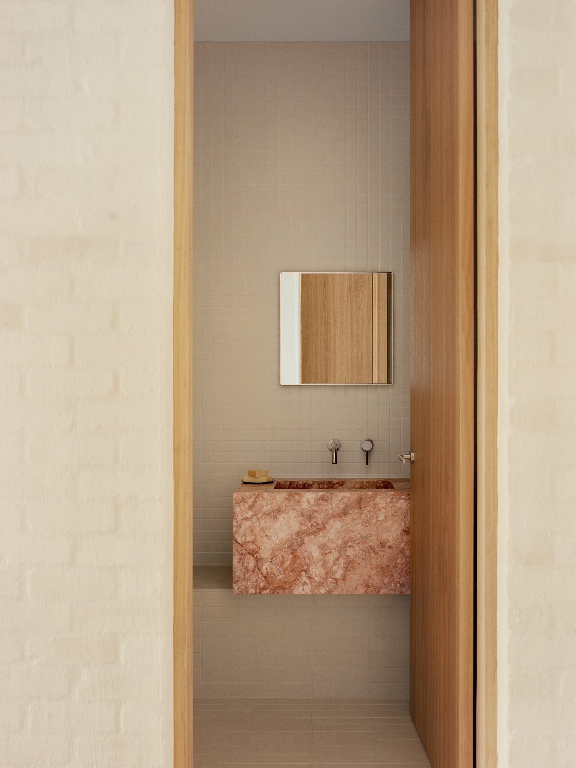 View through timber doorway to a powder room with cantilevered pink stone basin
