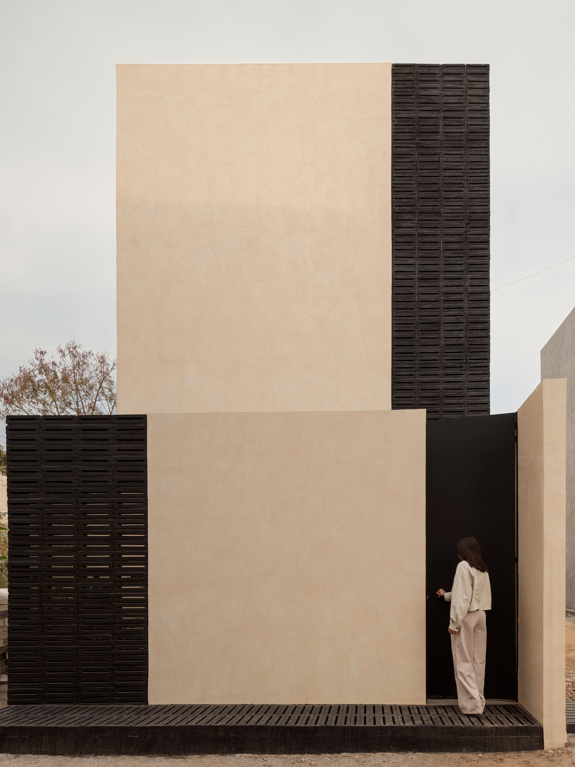 Exterior facade composition of cream plaster and dark textured brick with a figure entering an opening