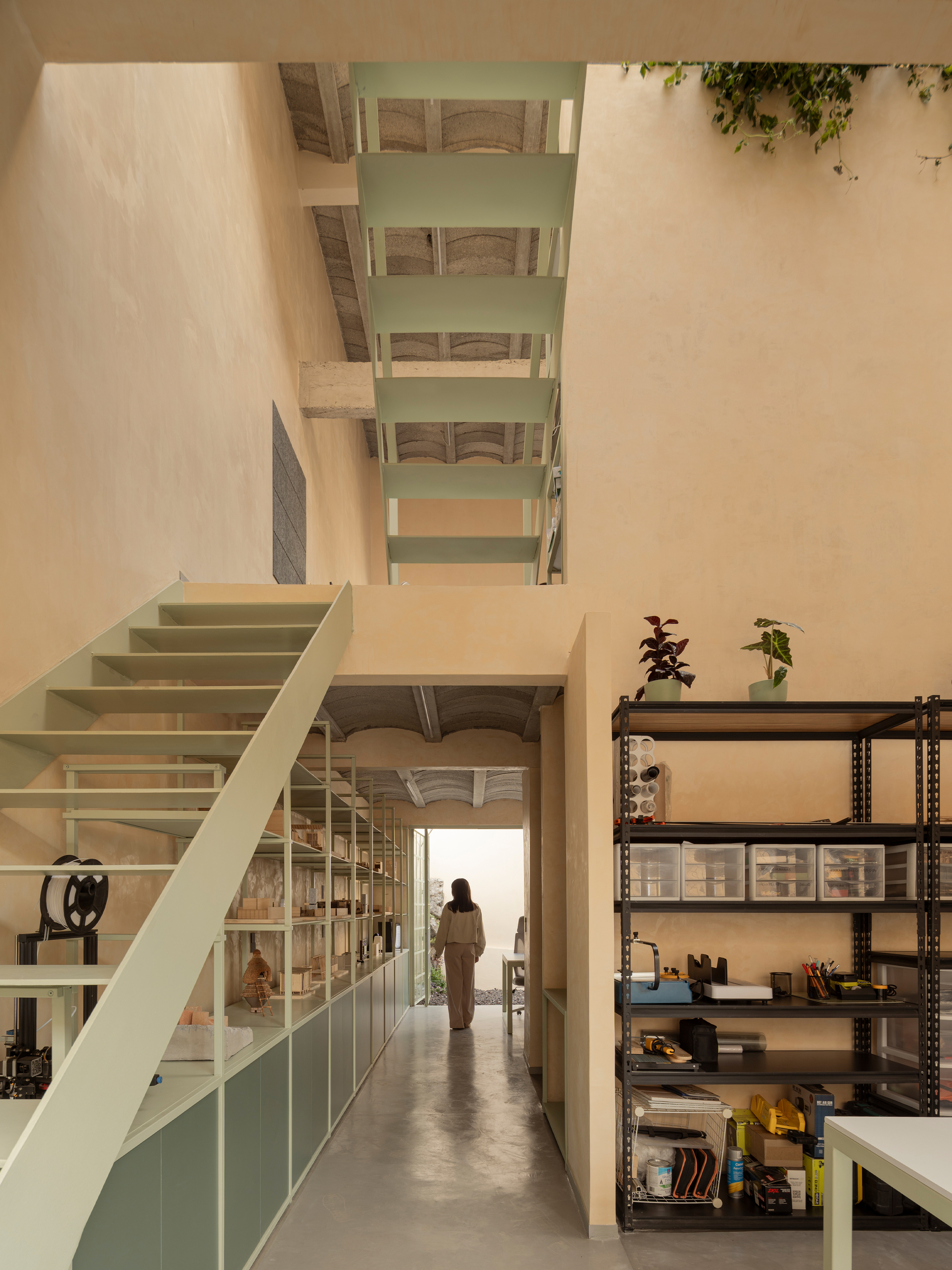 Interior hallway with pale green staircase rising to a skylight above a person walking toward sunlit entry