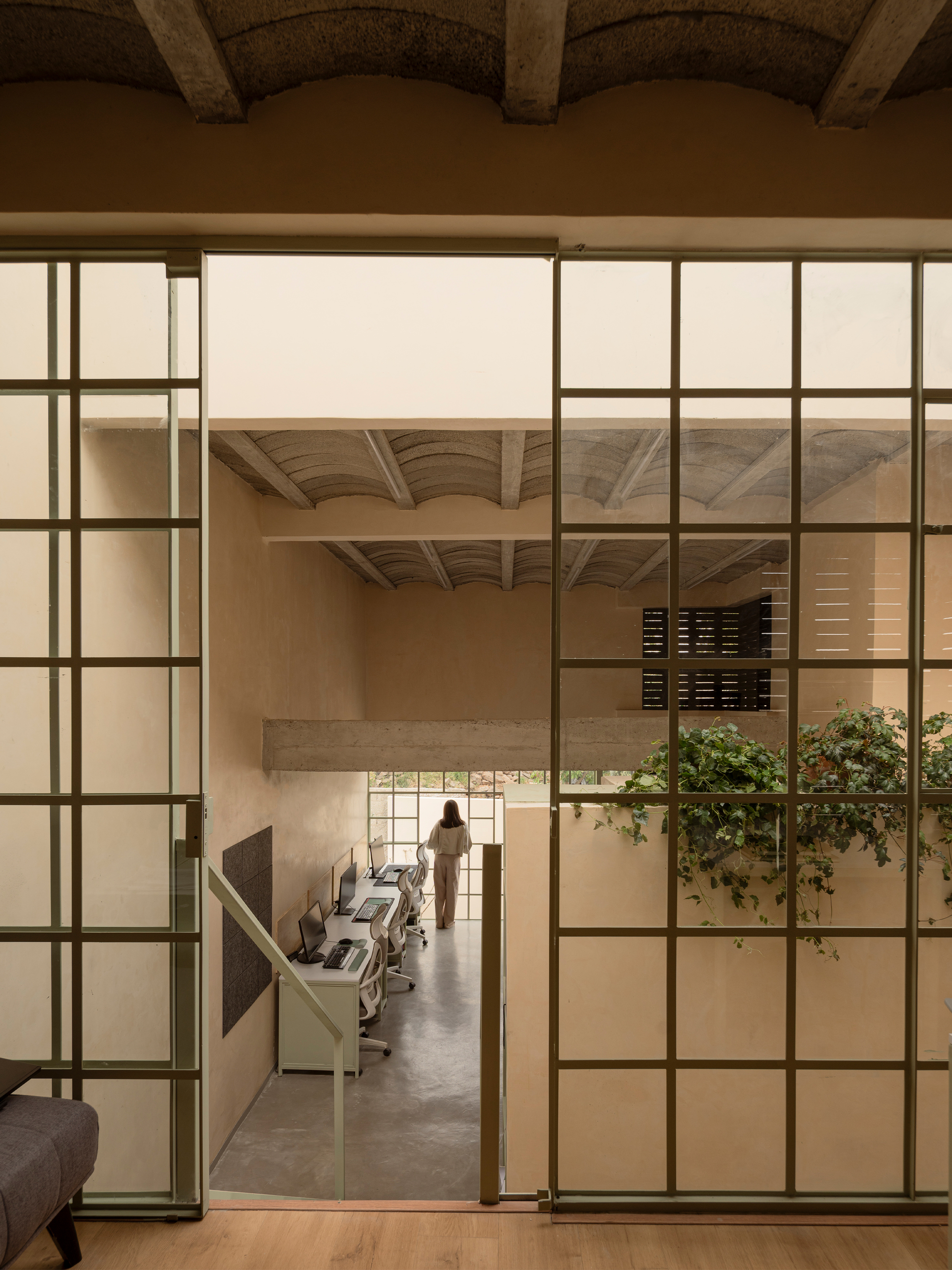 View through steel-framed glazed partition into workspace with vaulted ceiling and figure at far window