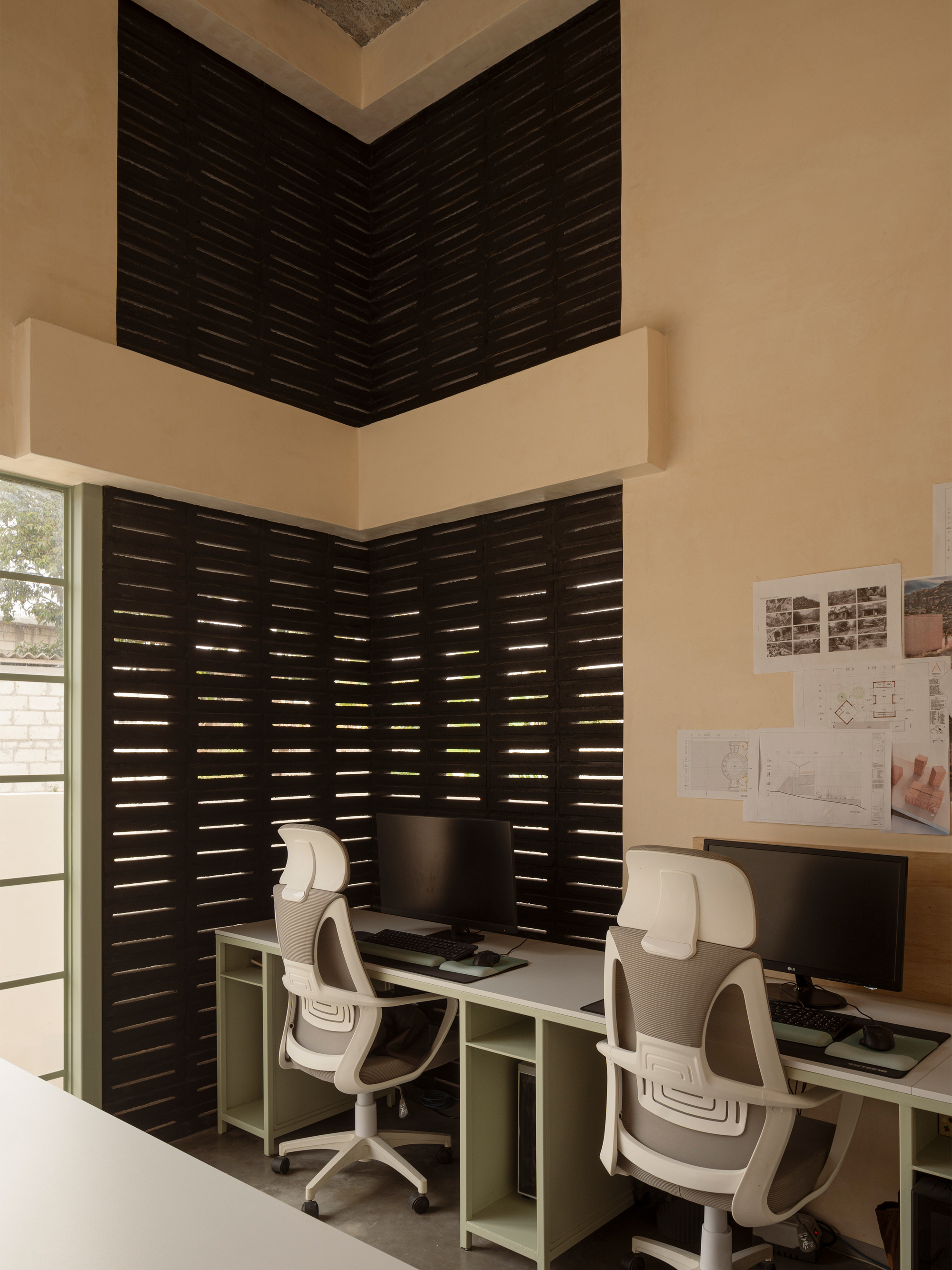 Double-height workspace corner with horizontal louvered screens and pinned drawings on the wall